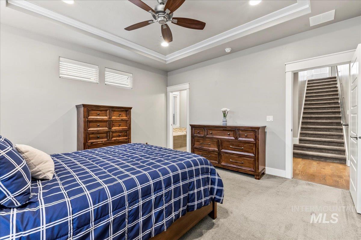 Carpeted bedroom with a tray ceiling, a ceiling fan, connected bathroom, and recessed lighting