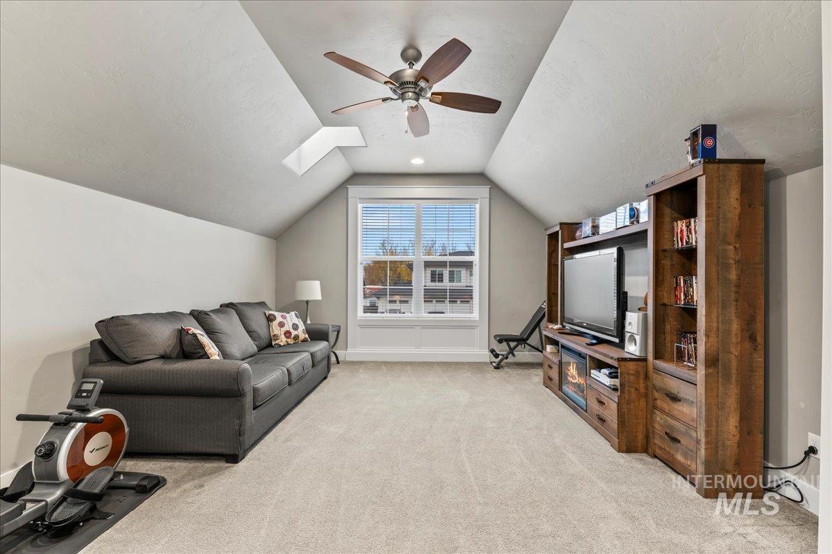 Living room with a textured ceiling, light carpet, lofted ceiling, ceiling fan, and a skylight