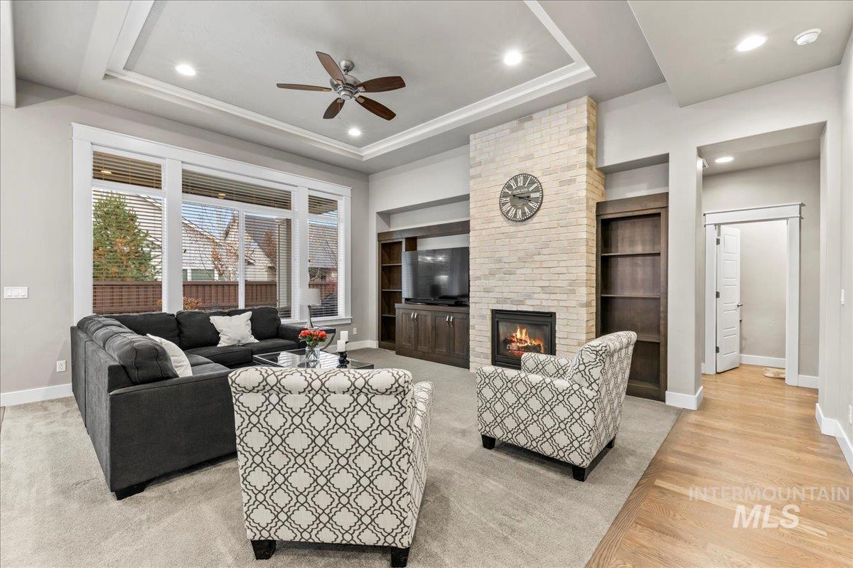 Living room with recessed lighting, a brick fireplace, a ceiling fan, a tray ceiling, and built in features