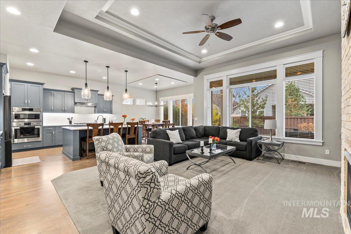Living area with a raised ceiling, healthy amount of natural light, recessed lighting, and ceiling fan
