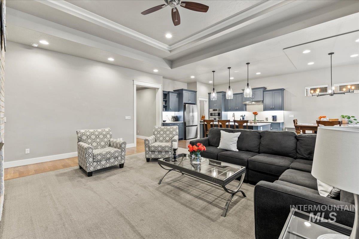 Living room featuring recessed lighting, light wood-type flooring, ceiling fan, and a tray ceiling
