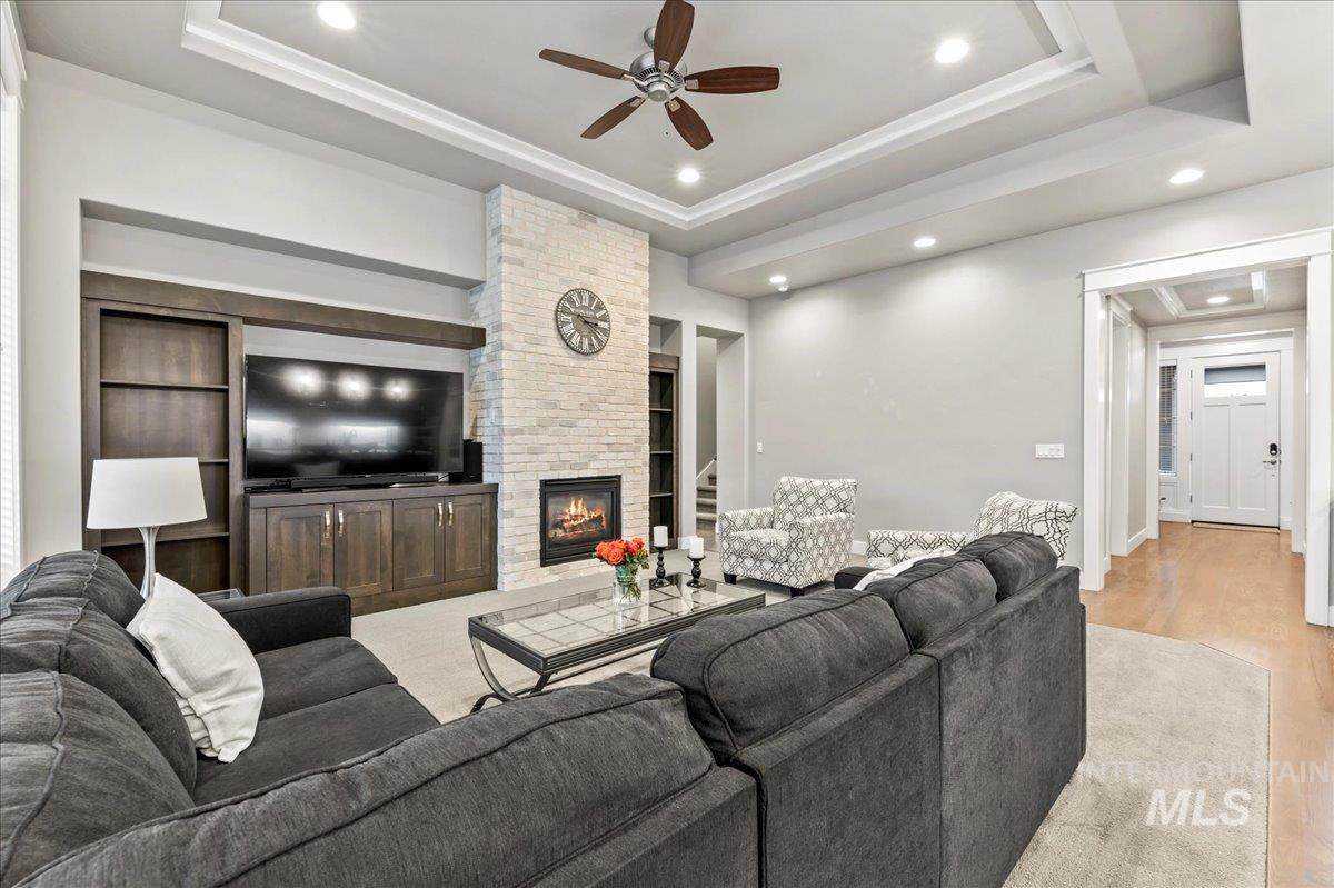 Living room featuring a tray ceiling, recessed lighting, a fireplace, light wood finished floors, and a ceiling fan