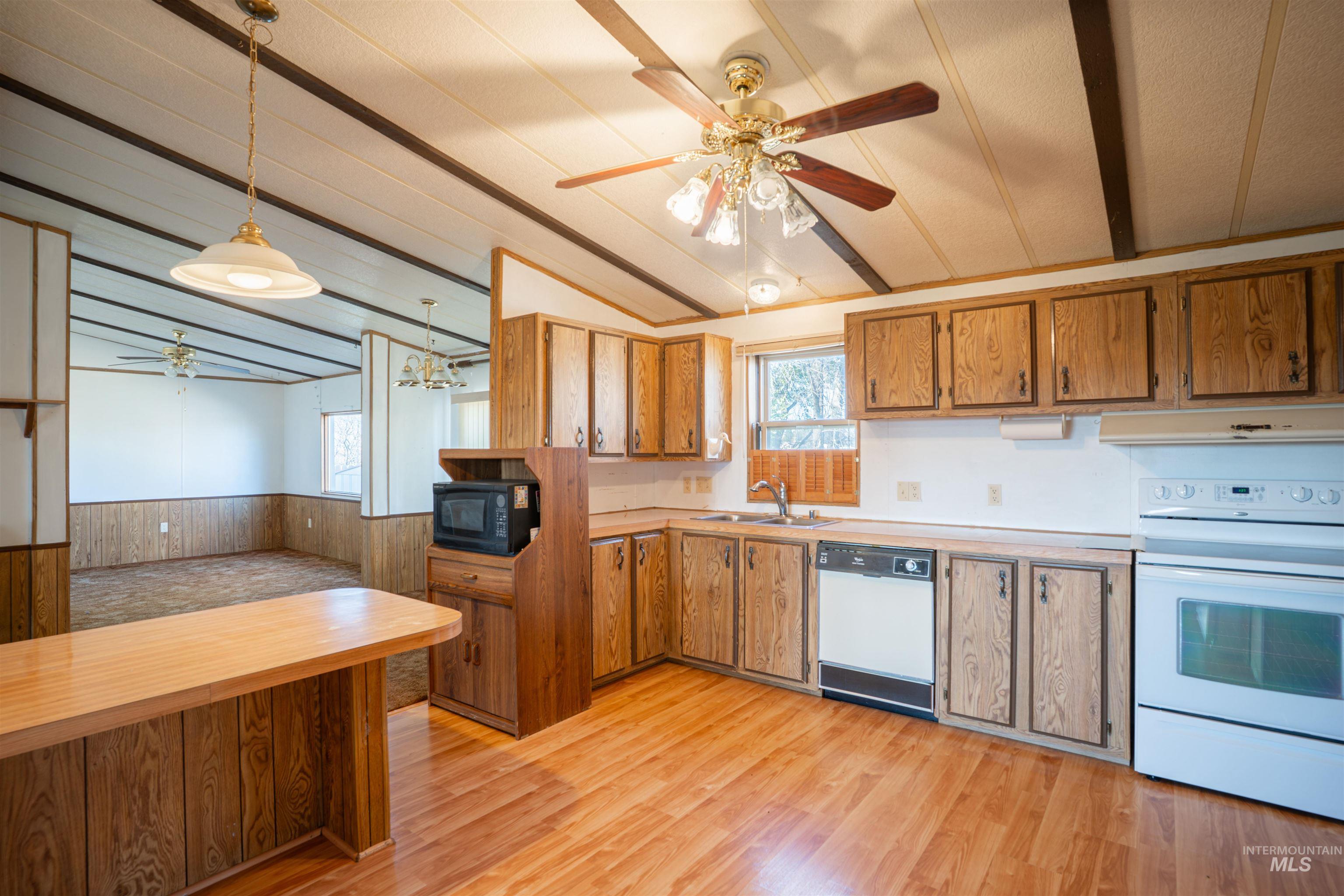 Kitchen featuring ceiling fan, white appliances, a wainscoted wall, light countertops, and light wood-style floors