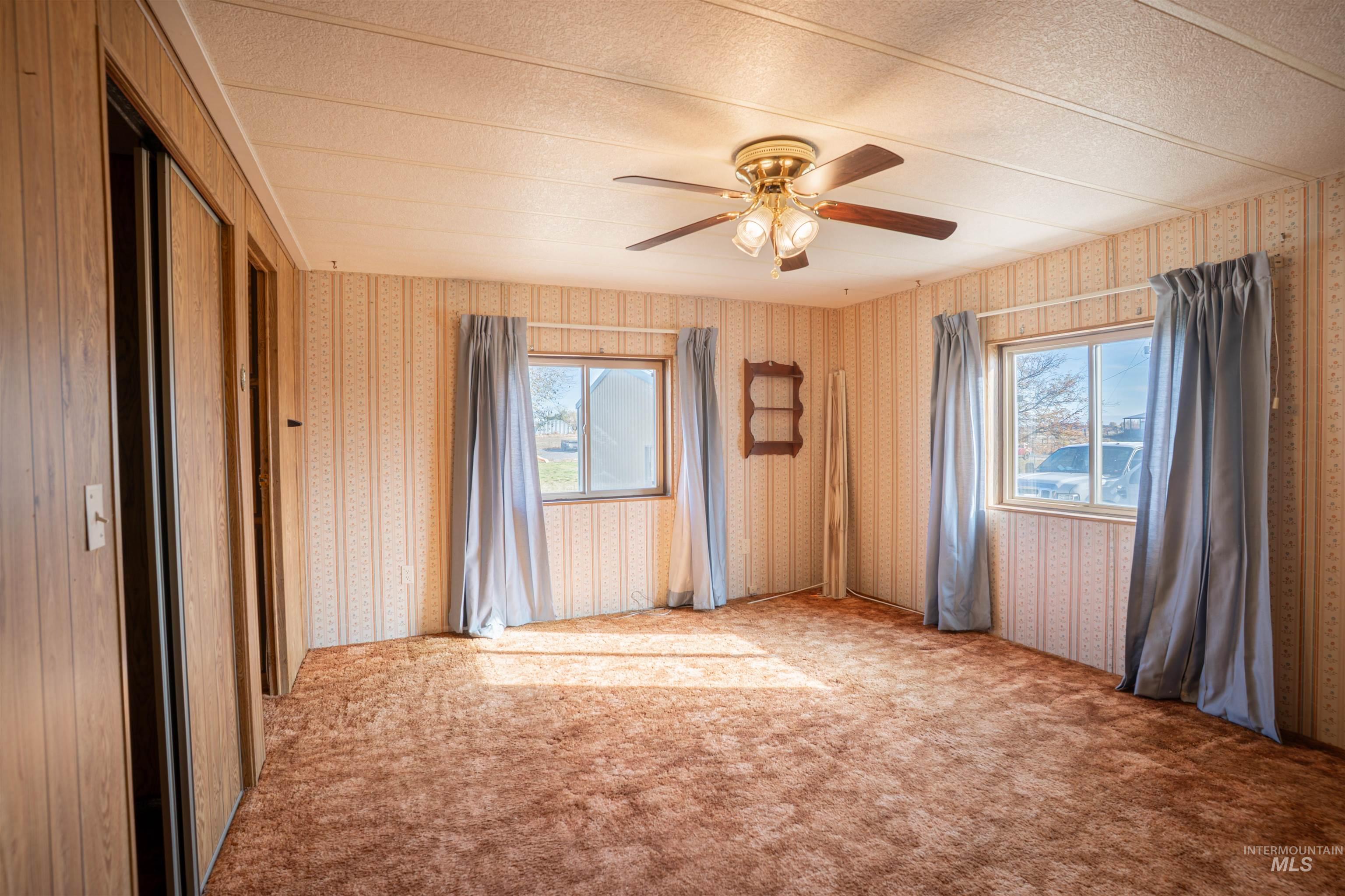 Carpeted empty room with plenty of natural light, wallpapered walls, ceiling fan, and a textured ceiling