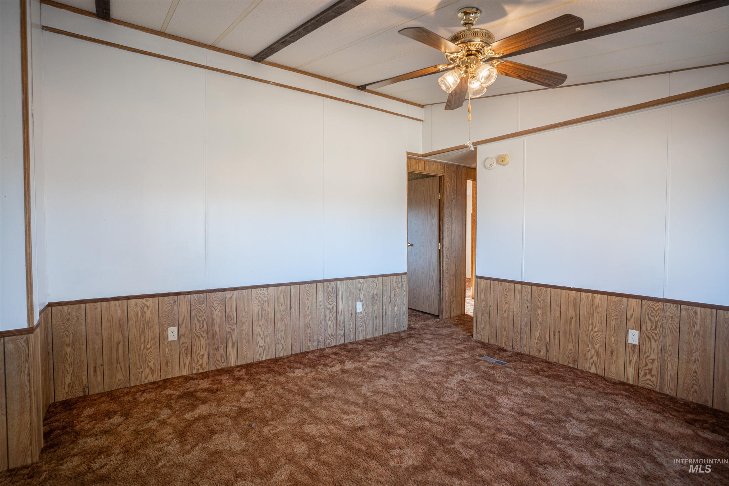 Unfurnished room with wooden walls, dark colored carpet, a wainscoted wall, and a ceiling fan