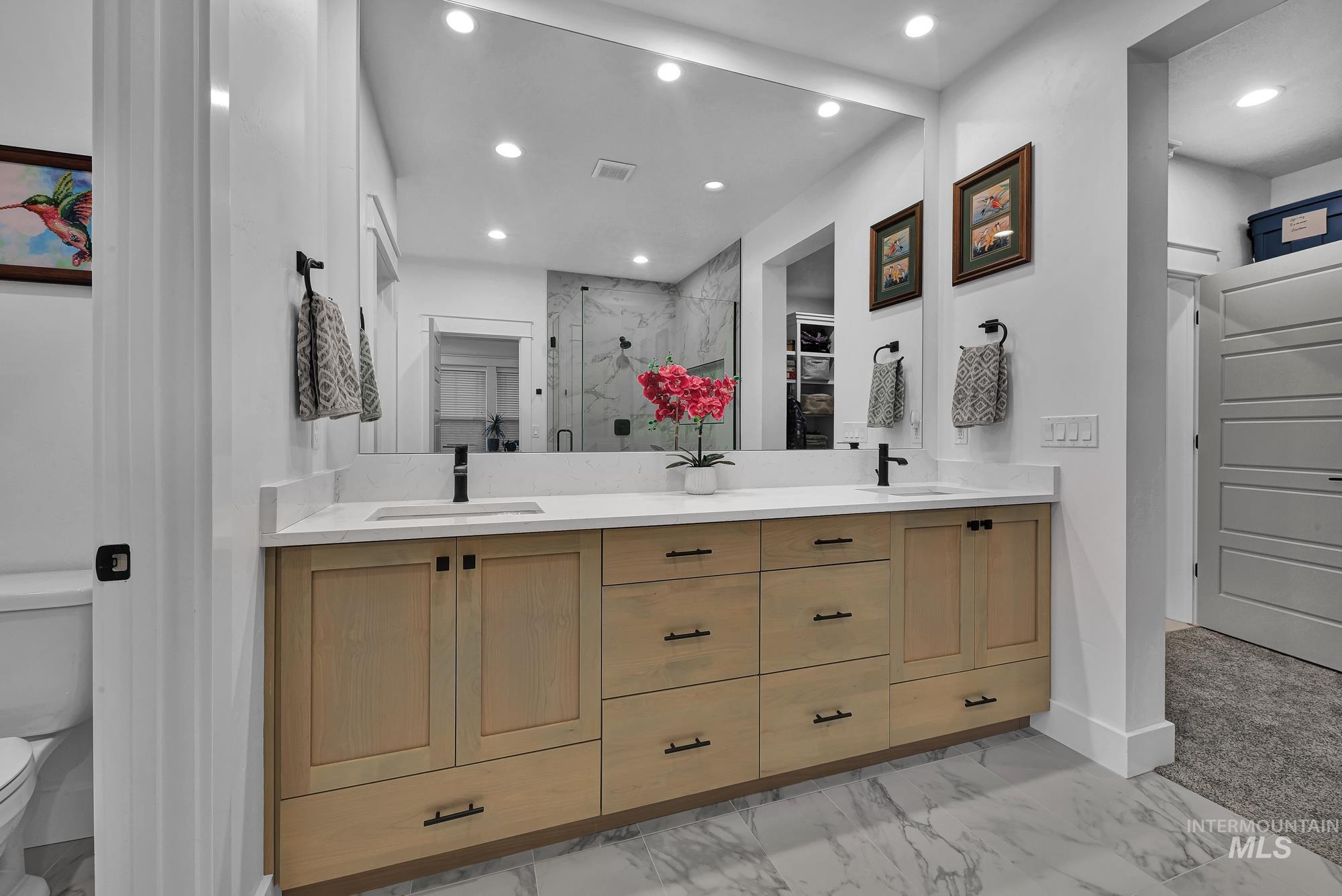 Full bath with double vanity, a marble finish shower, light marble finish flooring, a walk in closet, and recessed lighting