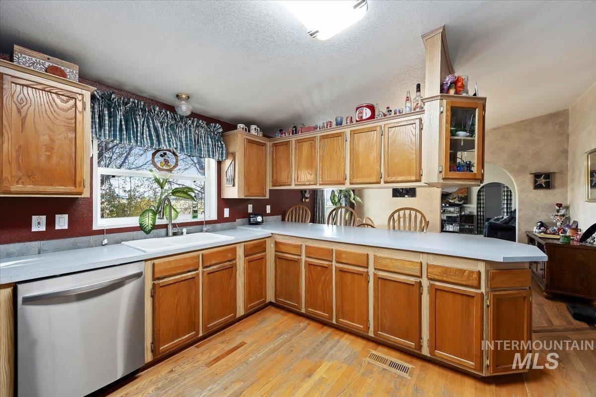 Kitchen with stainless steel dishwasher, a peninsula, light countertops, light wood-style flooring, and a textured ceiling