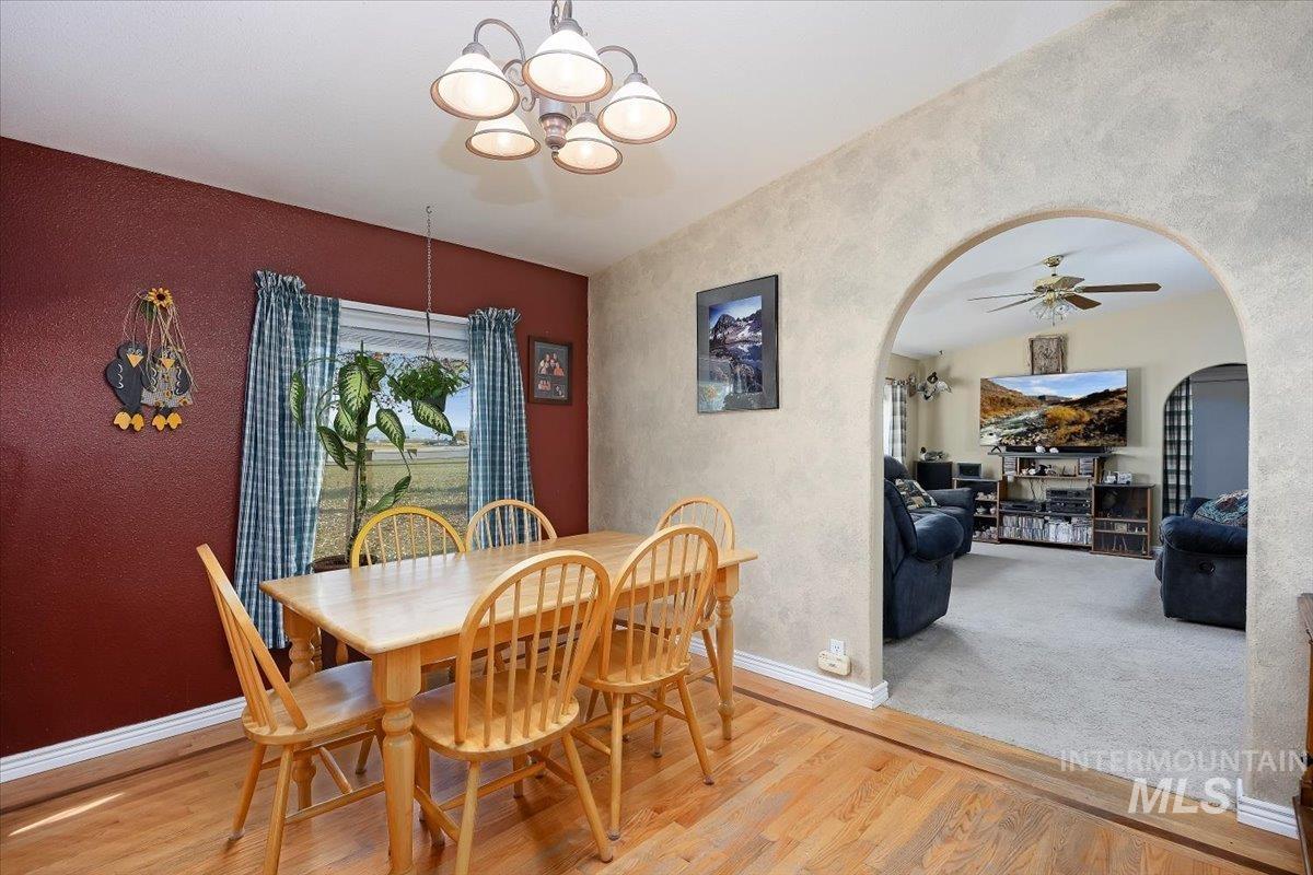 Dining space featuring light wood-style floors, a textured wall, arched walkways, a ceiling fan, and a chandelier