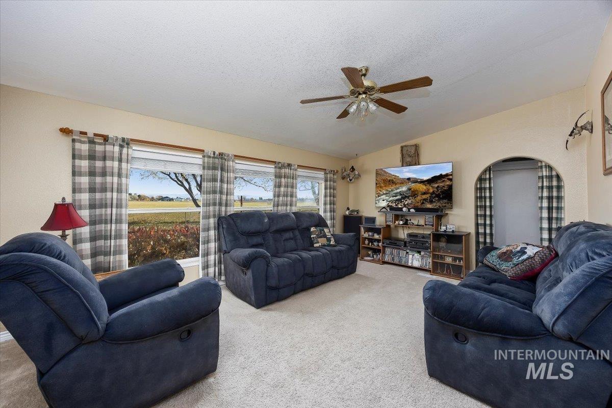 Carpeted living room with vaulted ceiling, a textured ceiling, and a ceiling fan