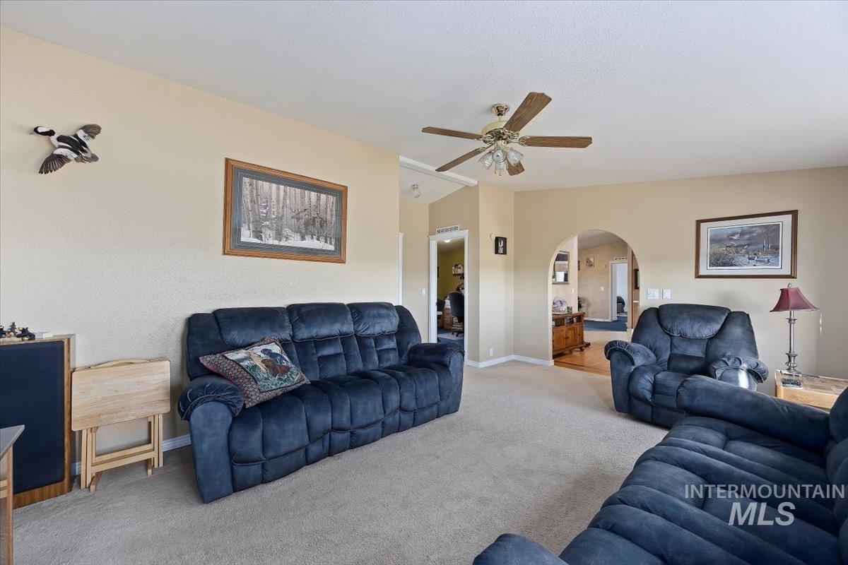 Carpeted living area featuring arched walkways, ceiling fan, and vaulted ceiling