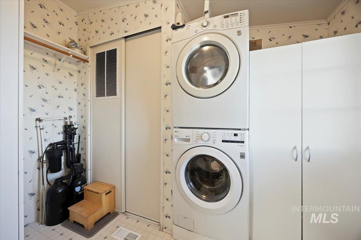 Laundry area with wallpapered walls, stacked washer / dryer, and ornamental molding