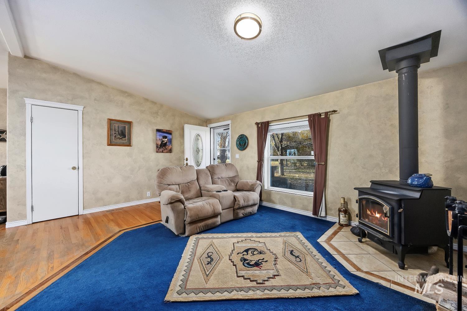 Living area with a wood stove, lofted ceiling, a textured ceiling, and wood finished floors