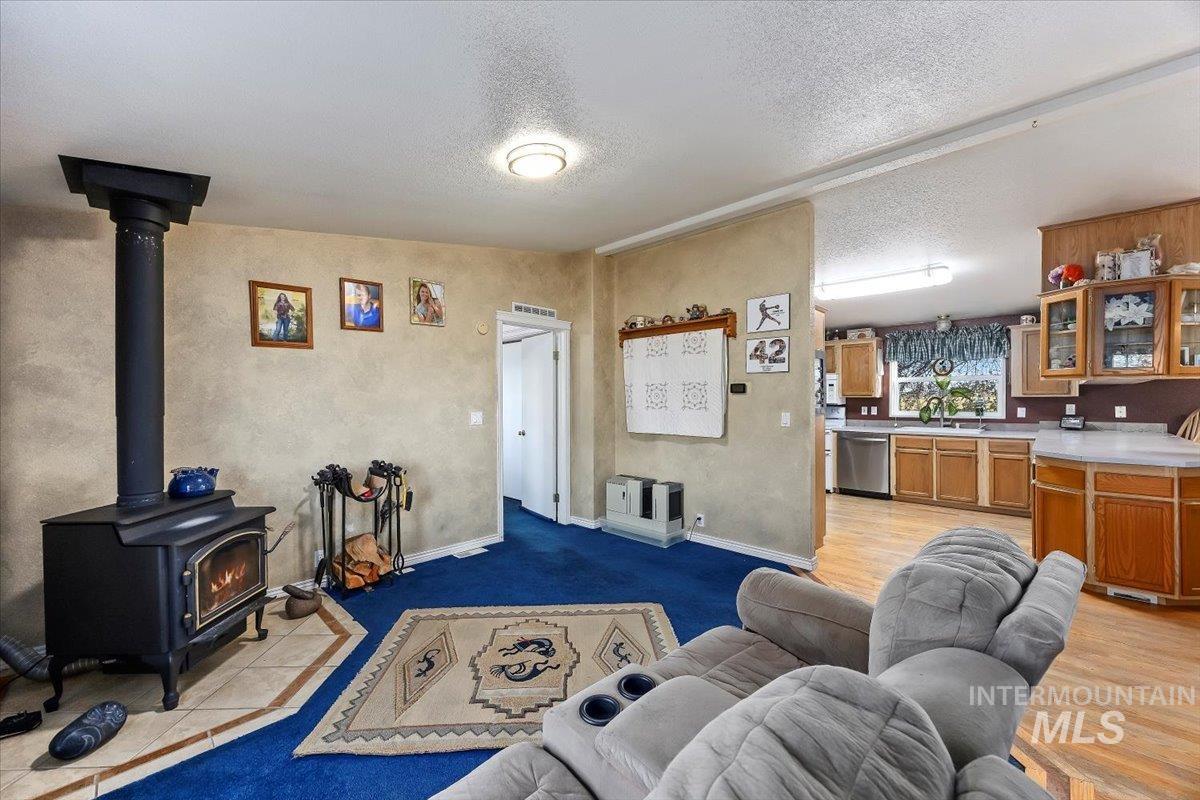 Living room featuring a wood stove, a textured ceiling, light tile patterned floors, and a textured wall