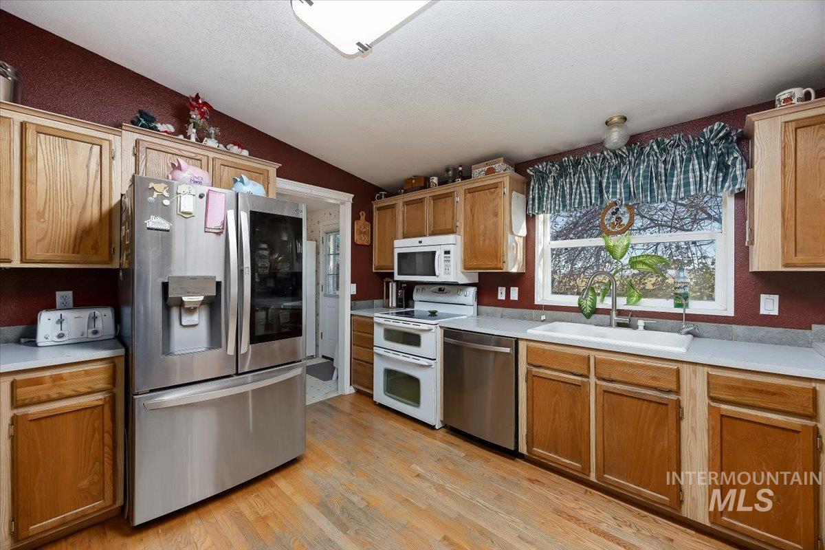 Kitchen featuring stainless steel appliances, light countertops, light wood-style flooring, lofted ceiling, and a textured ceiling
