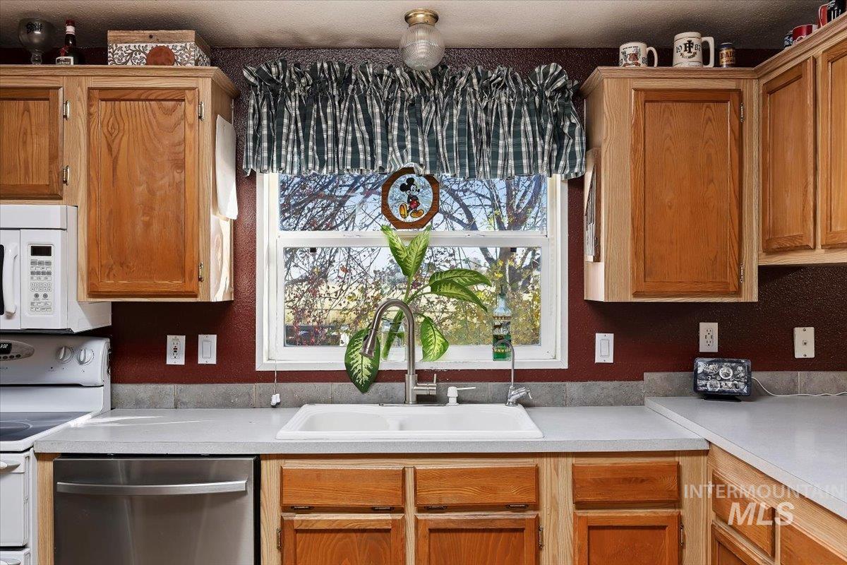 Kitchen featuring light countertops, white appliances, and brown cabinetry