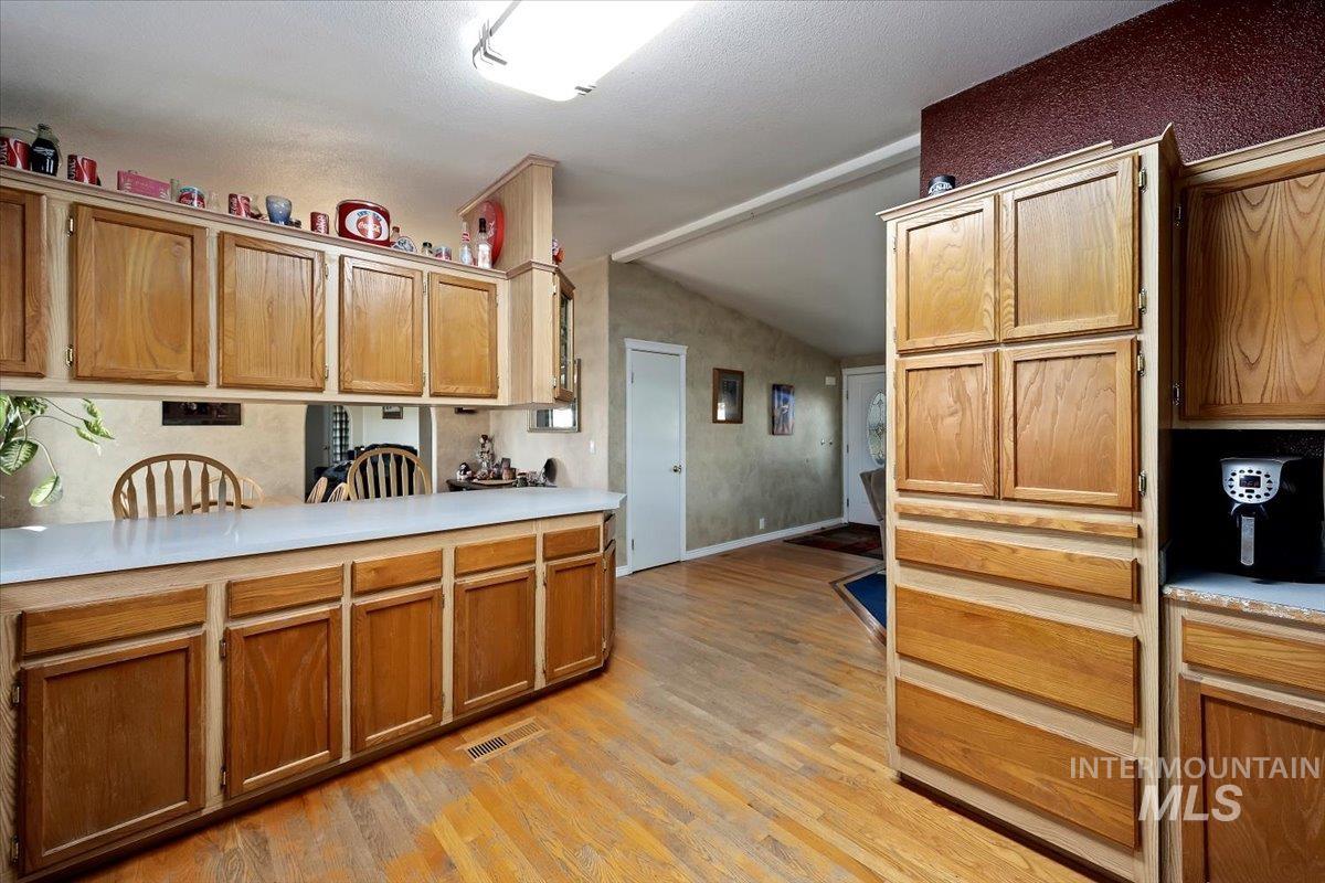 Kitchen featuring light countertops, light wood-type flooring, vaulted ceiling, and brown cabinets