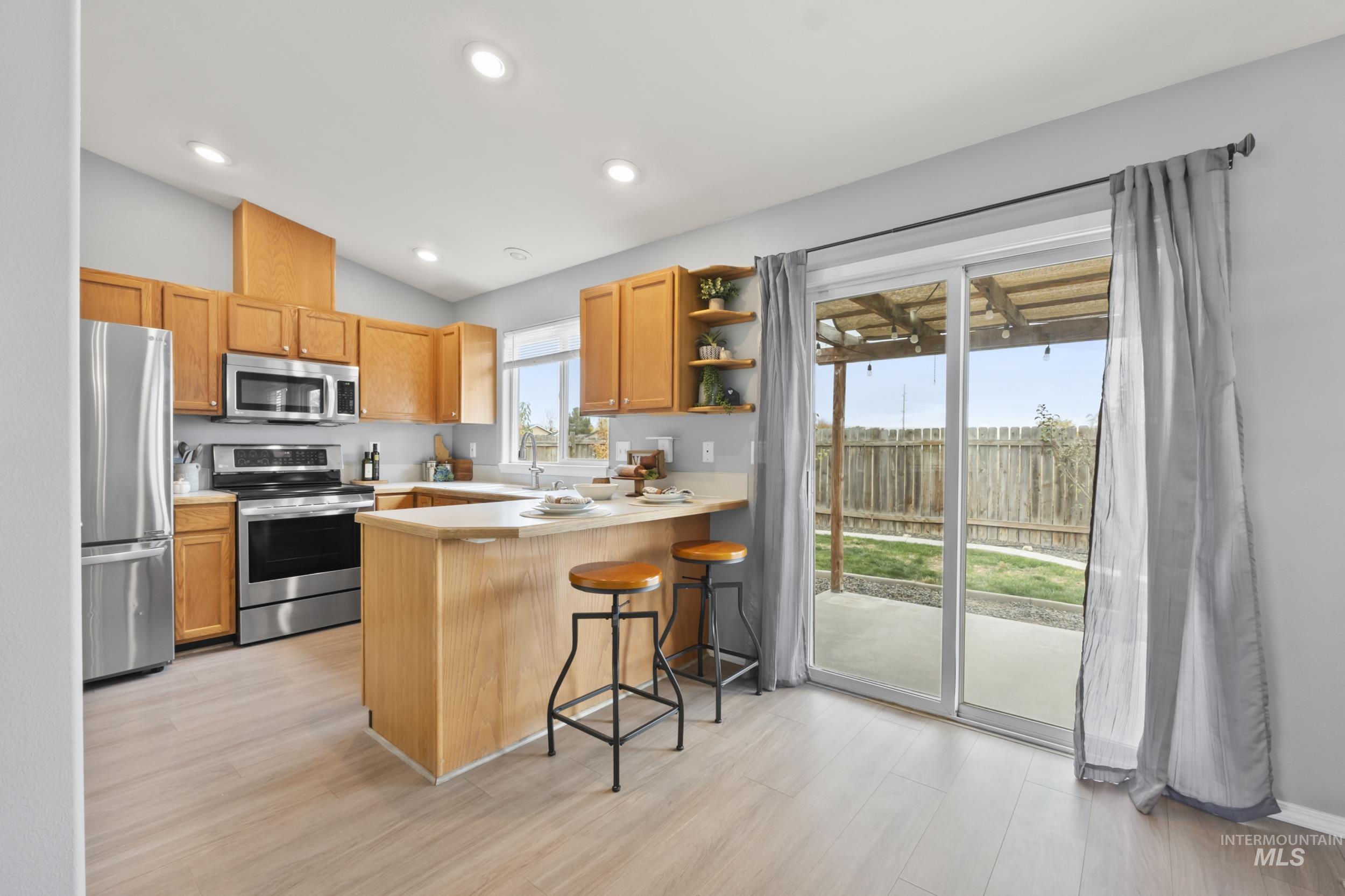 Kitchen with open shelves, stainless steel appliances, a breakfast bar area, a peninsula, and light wood finished floors