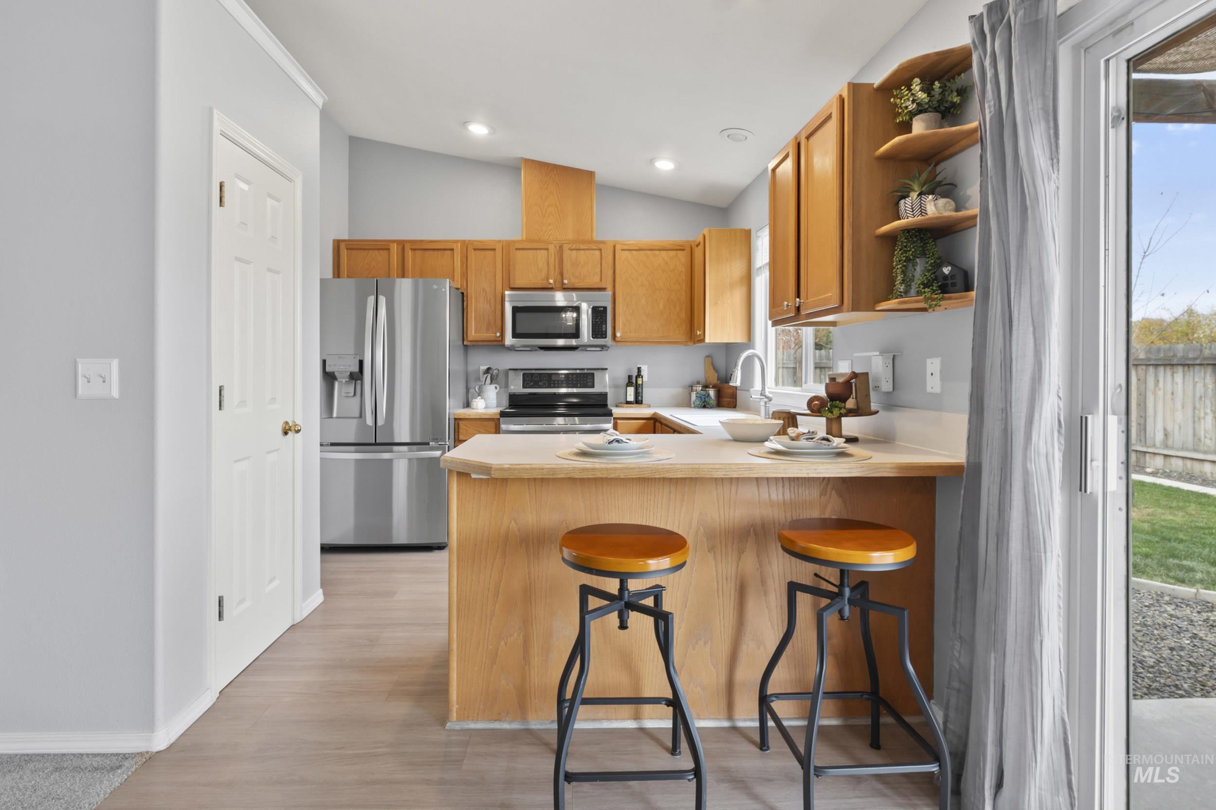 Kitchen featuring a breakfast bar area, light countertops, stainless steel appliances, a peninsula, and open shelves