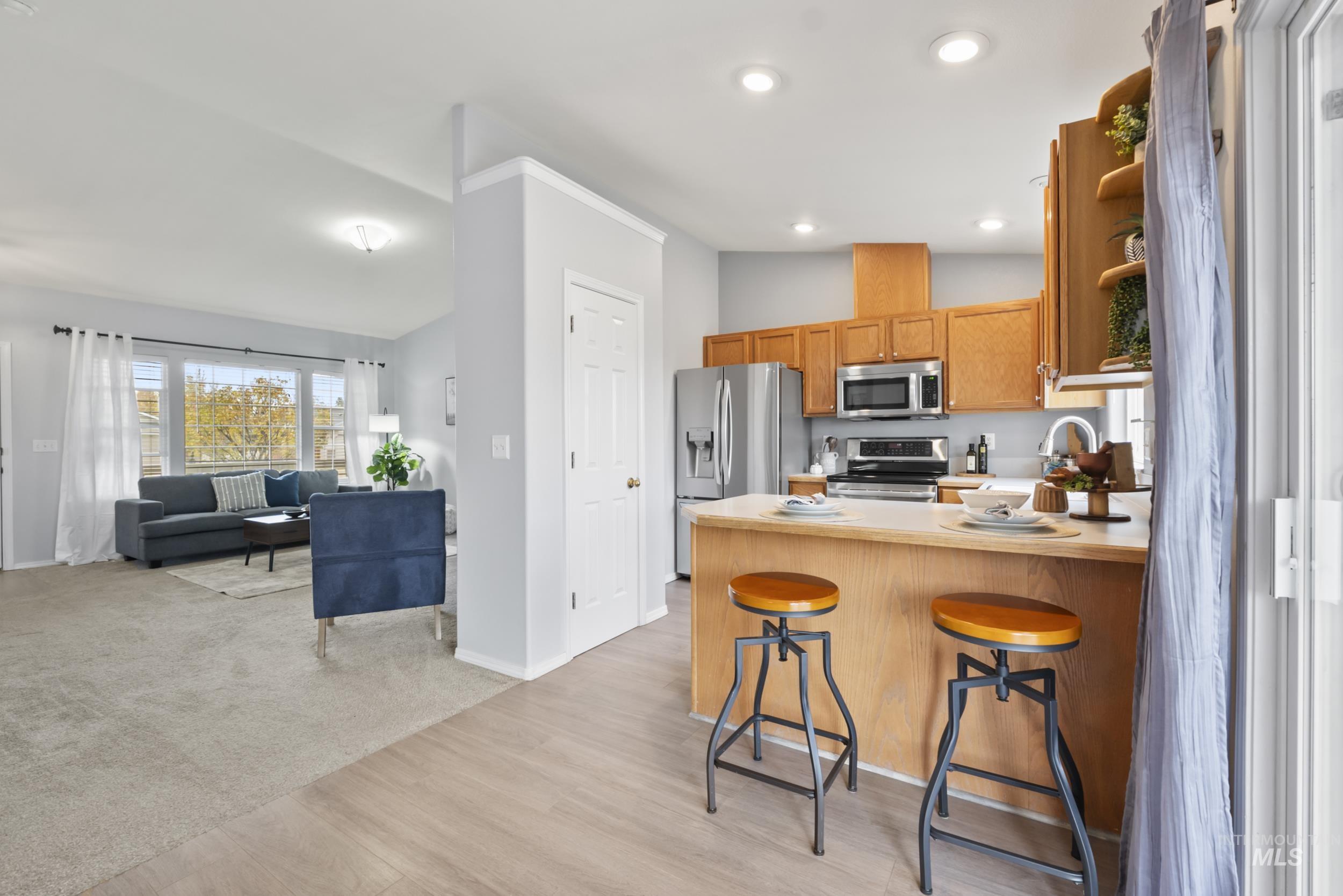 Kitchen with a breakfast bar area, a peninsula, brown cabinetry, appliances with stainless steel finishes, and light countertops