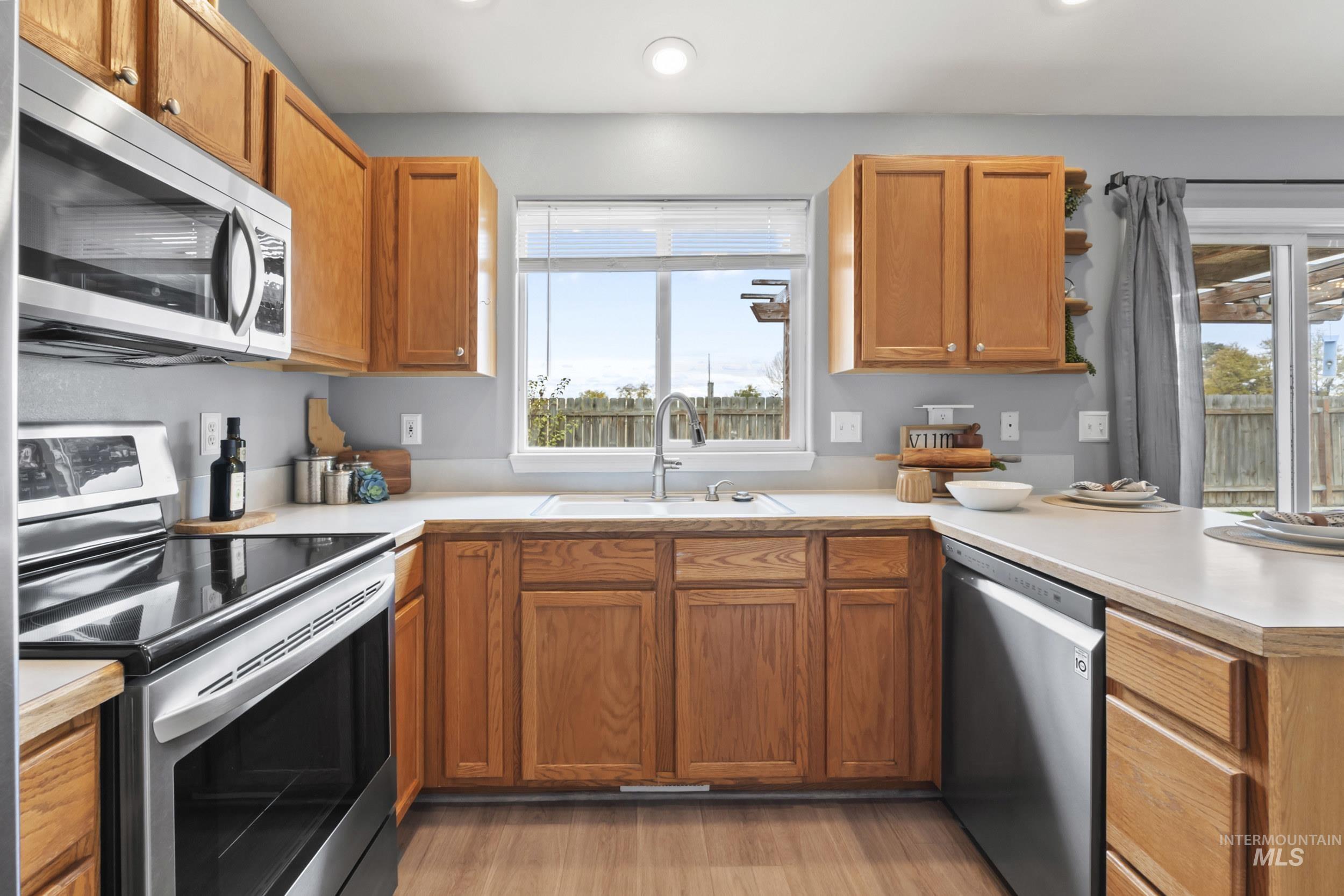 Kitchen featuring stainless steel appliances, light countertops, brown cabinetry, light wood-style flooring, and recessed lighting