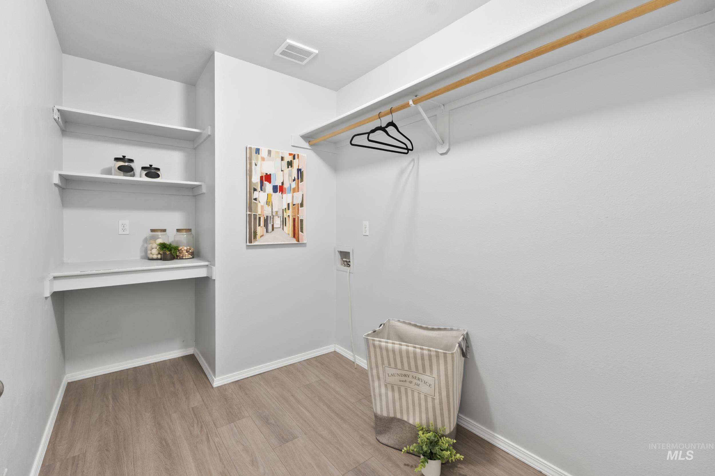 Spacious laundry room with shelving featuring light wood-style flooring