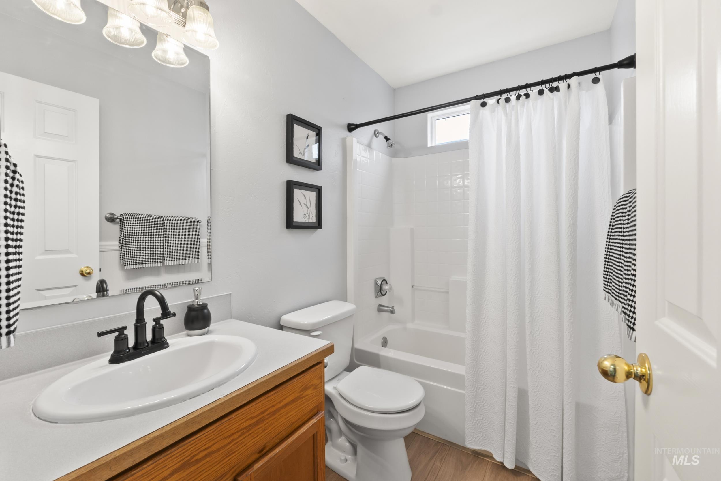 Full bath with shower / tub combo with curtain, vanity, and light wood-type flooring