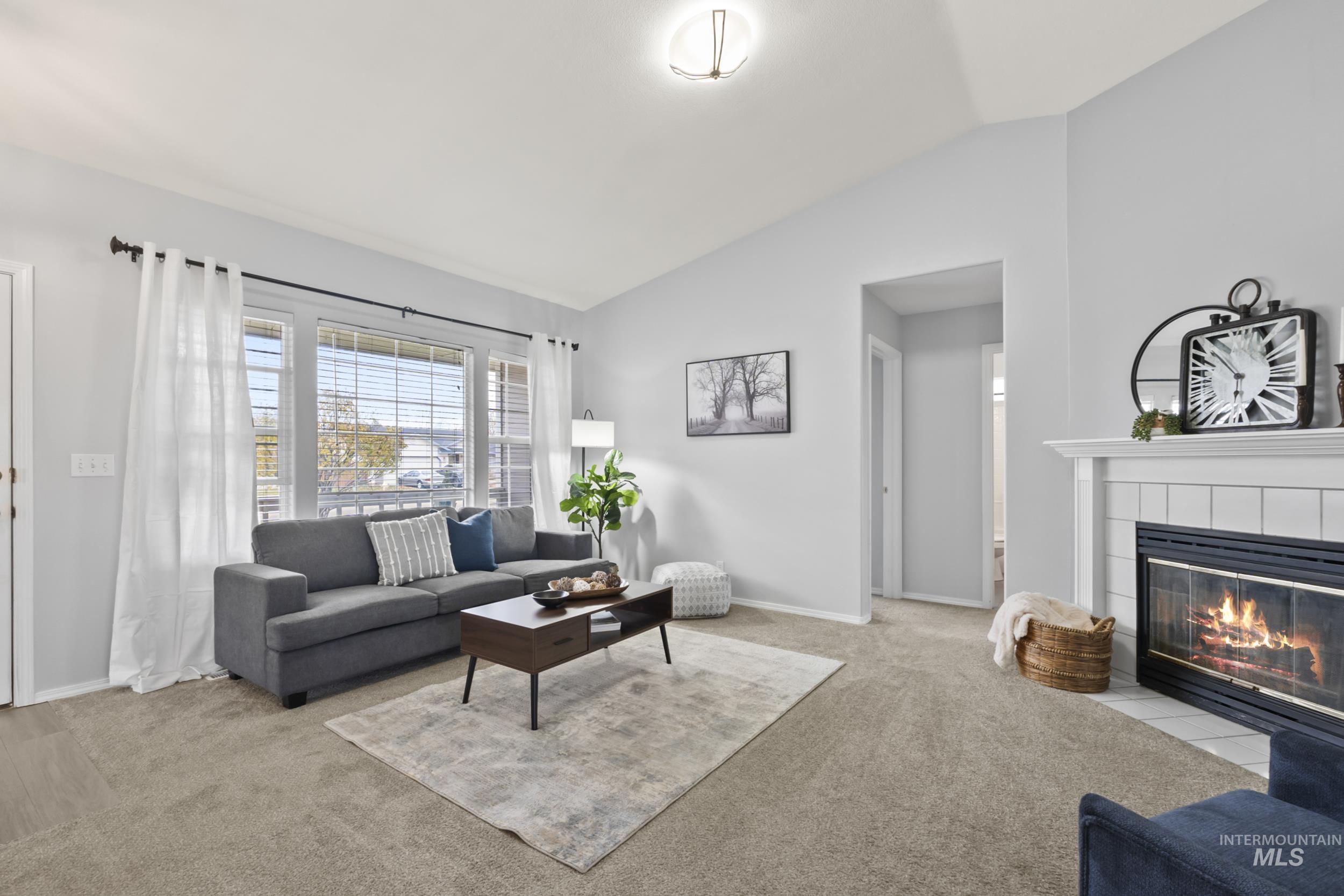 Living area with vaulted ceiling, light colored carpet, and a tiled fireplace