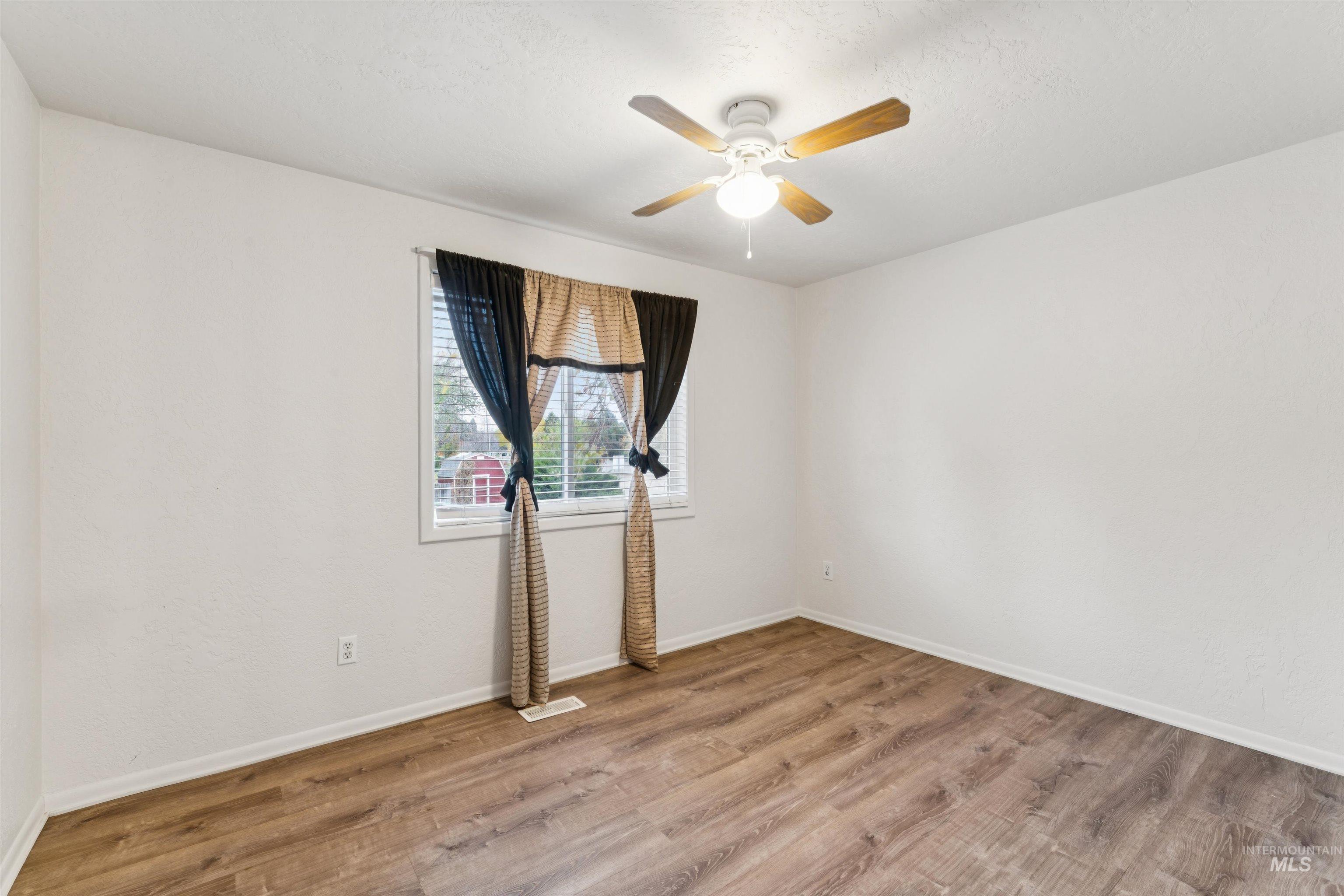 Empty room featuring light wood-style flooring, a ceiling fan, and a textured ceiling
