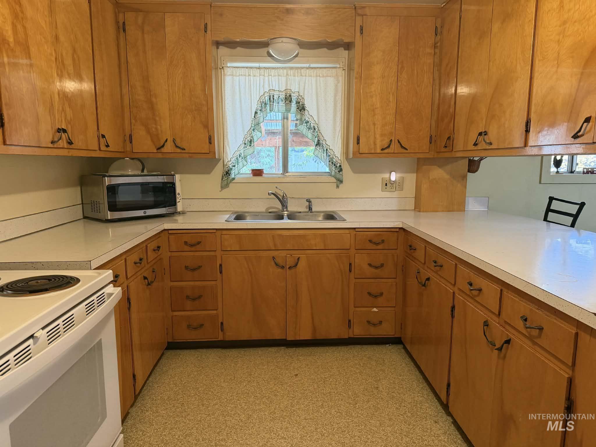 Kitchen with white electric range oven, brown cabinets, stainless steel microwave, and light countertops