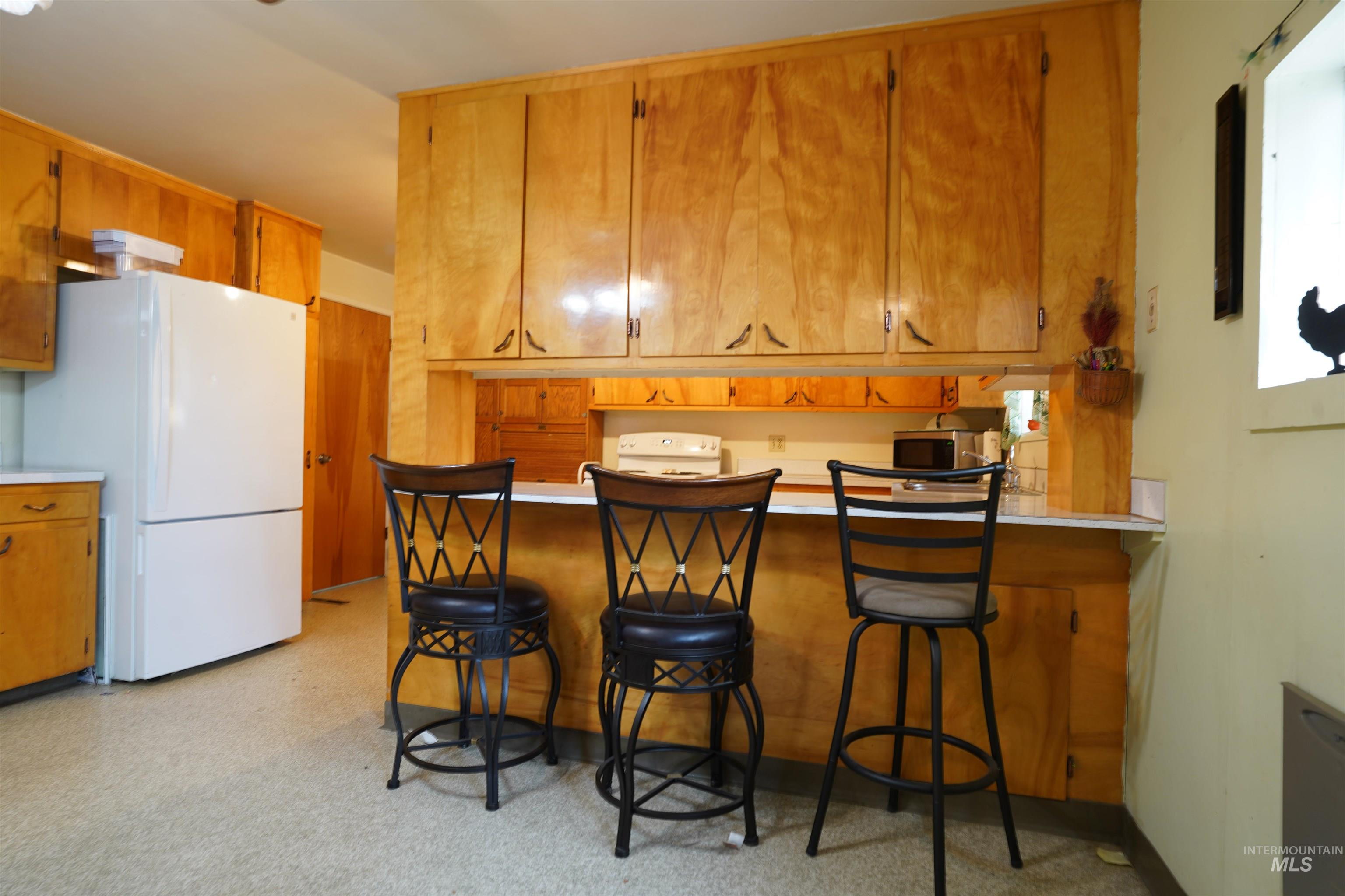 Kitchen featuring light countertops, white appliances, a breakfast bar area, and brown cabinetry