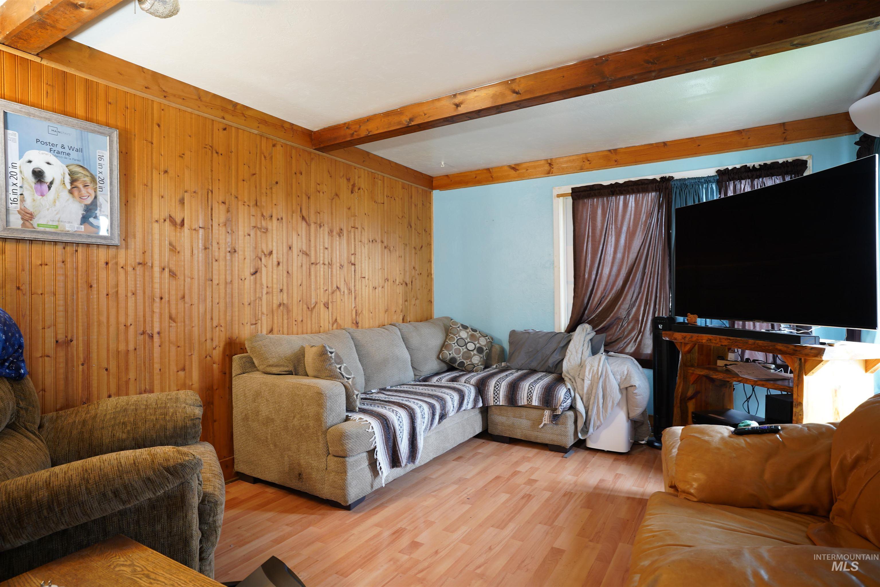 Living room with beam ceiling, wooden walls, and wood finished floors