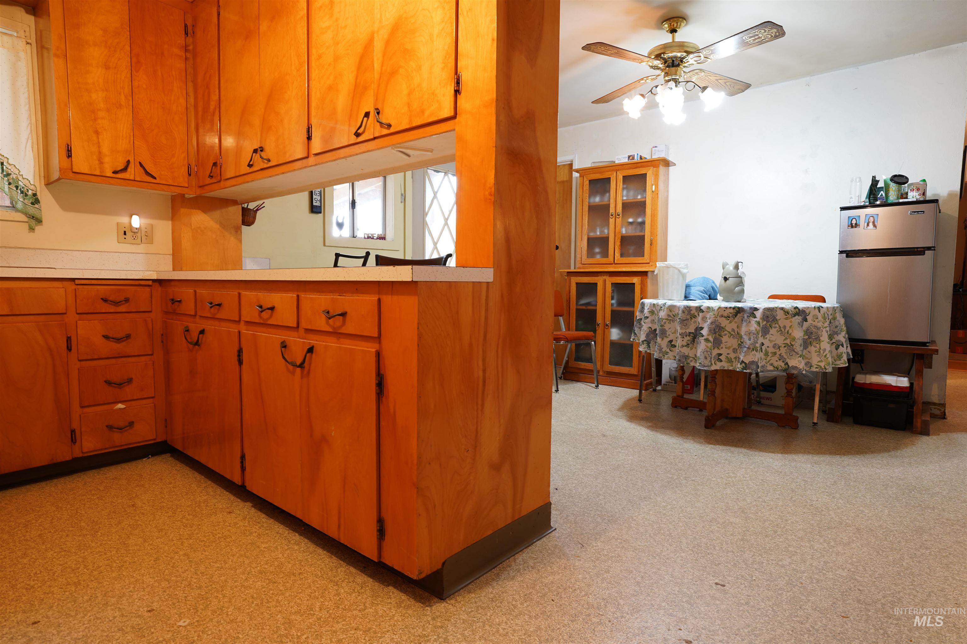 Kitchen with light countertops, freestanding refrigerator, brown cabinets, ceiling fan, and light flooring