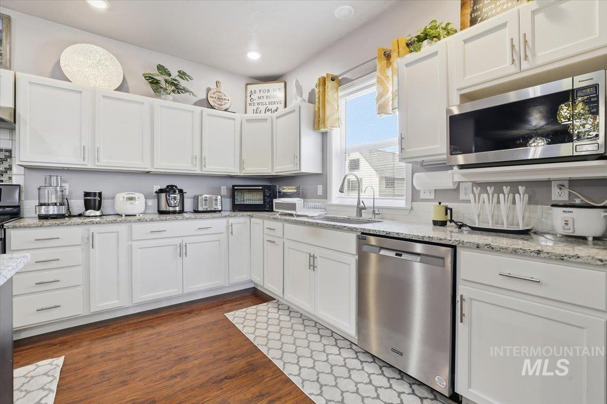 Kitchen with white cabinetry, stainless steel appliances, light stone counters, dark wood-style flooring, and recessed lighting
