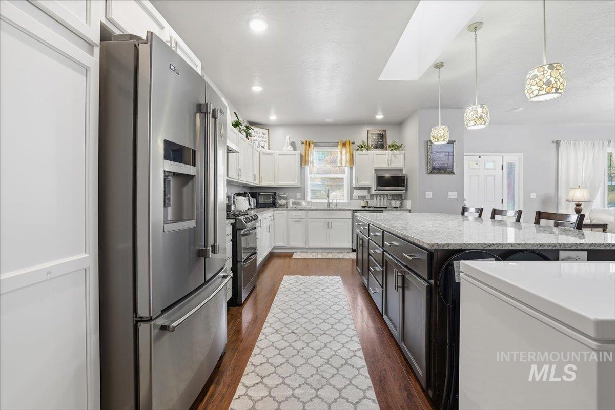 Kitchen with appliances with stainless steel finishes, white cabinets, dark wood-style floors, a kitchen breakfast bar, and decorative light fixtures