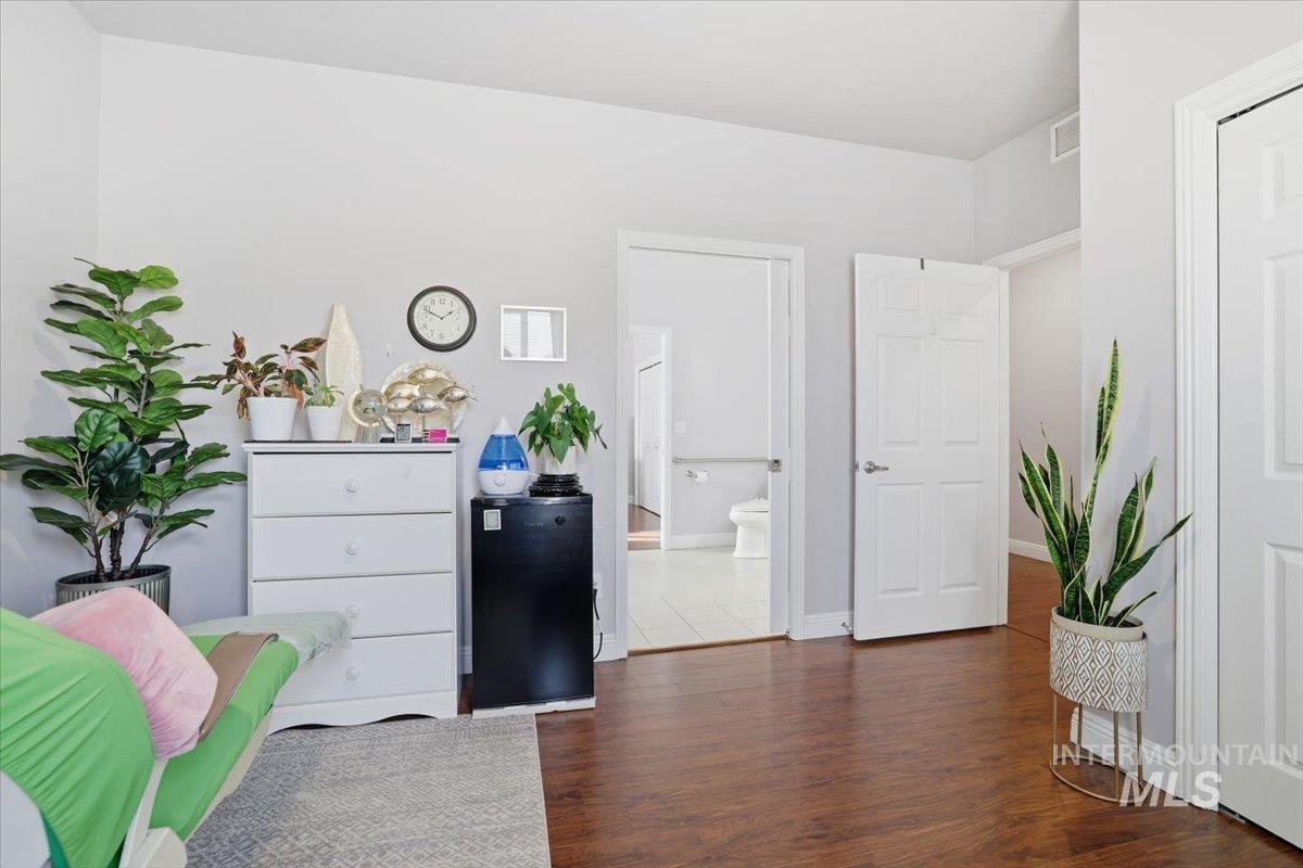 Bedroom with dark wood-style flooring, black fridge, and ensuite bath