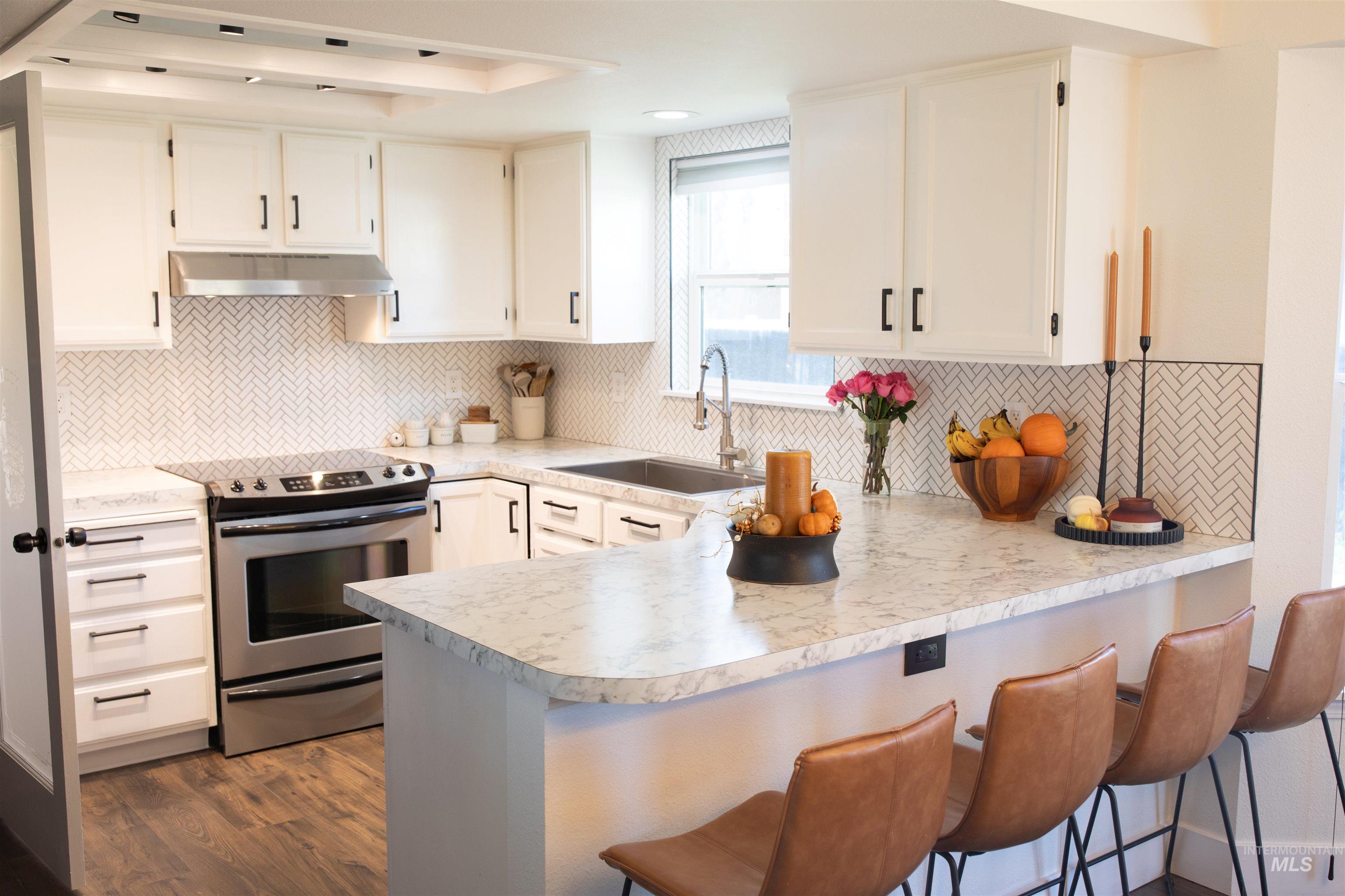 Kitchen featuring electric stove, a breakfast bar and an under cabinet range hood