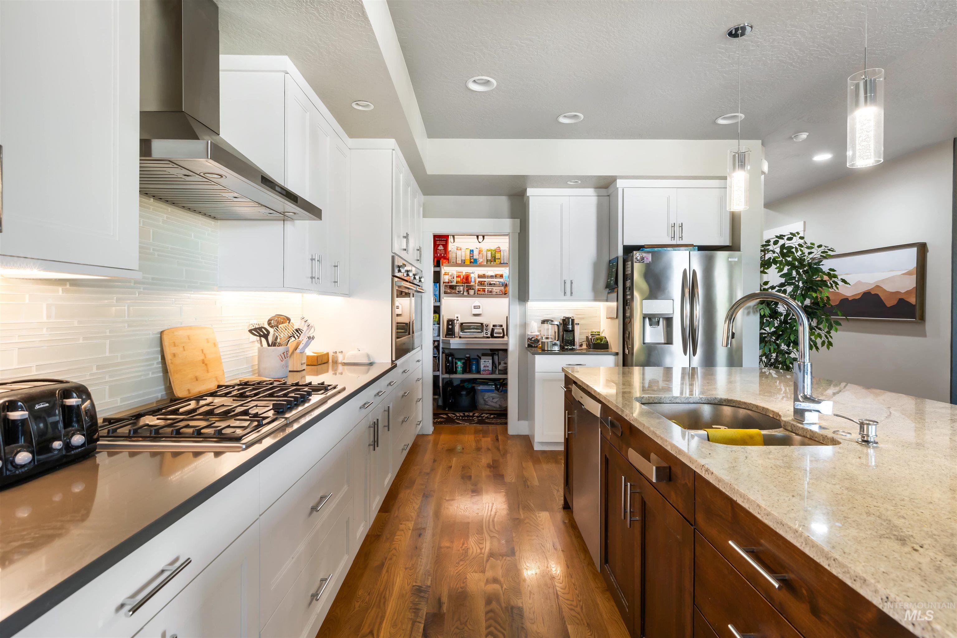 Kitchen featuring dark wood-style flooring, light stone counters, wall chimney exhaust hood, decorative backsplash, and recessed lighting