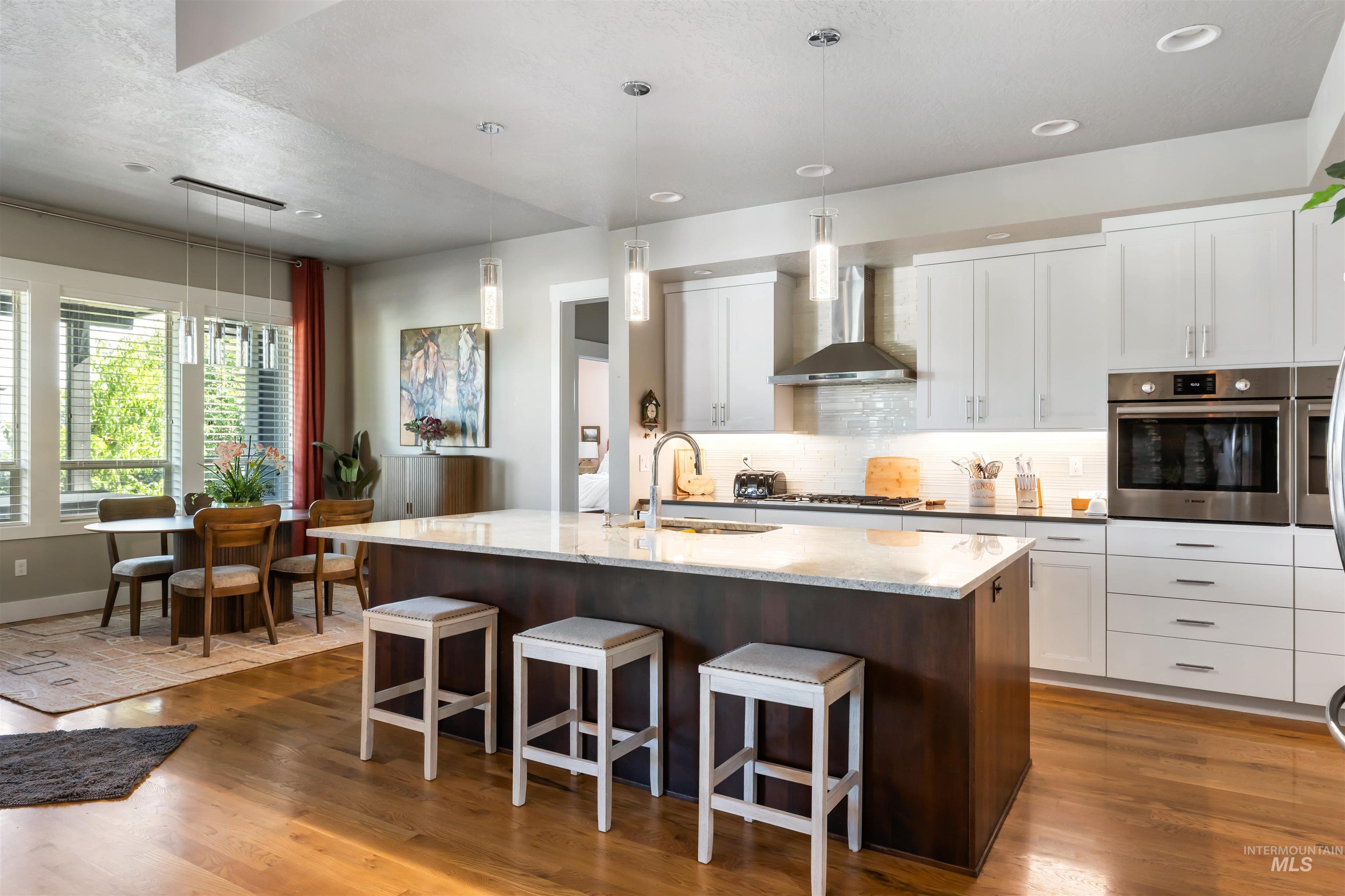 Kitchen featuring hanging light fixtures, tasteful backsplash, a kitchen breakfast bar, a center island with sink, and dark wood finished floors