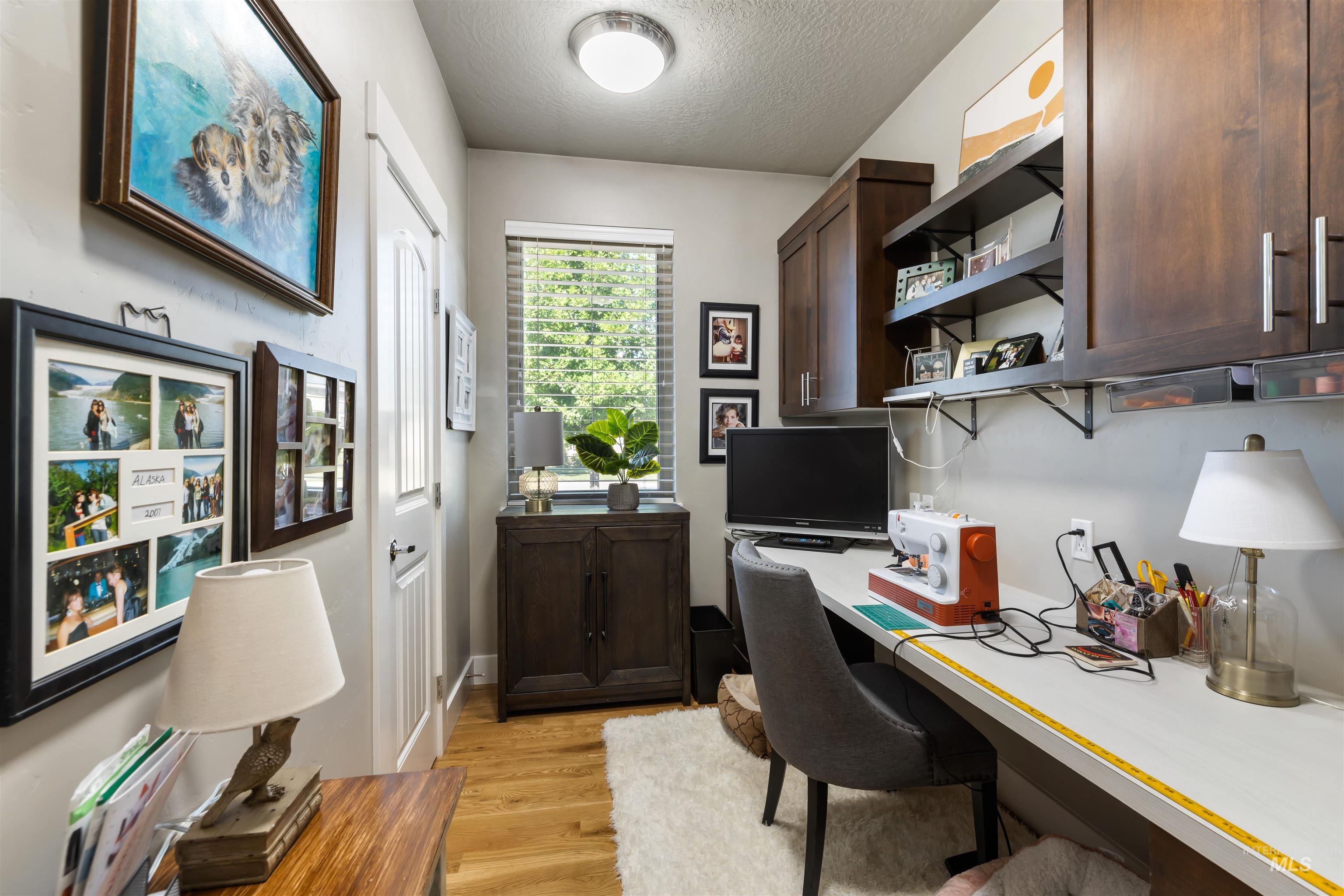 Home office with built in desk, a textured ceiling, and light wood-type flooring