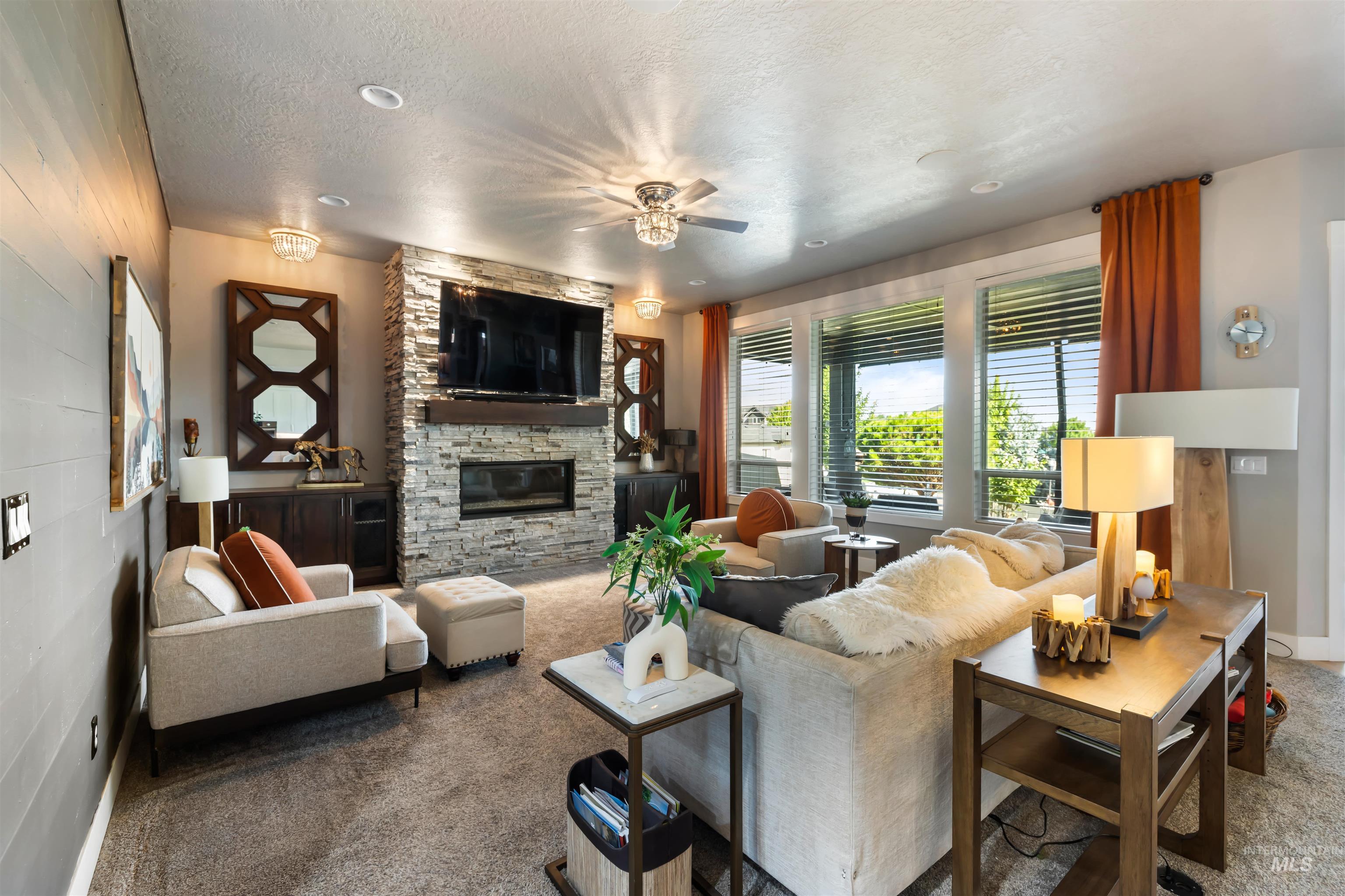 Carpeted living room featuring a stone fireplace, a textured ceiling, and ceiling fan