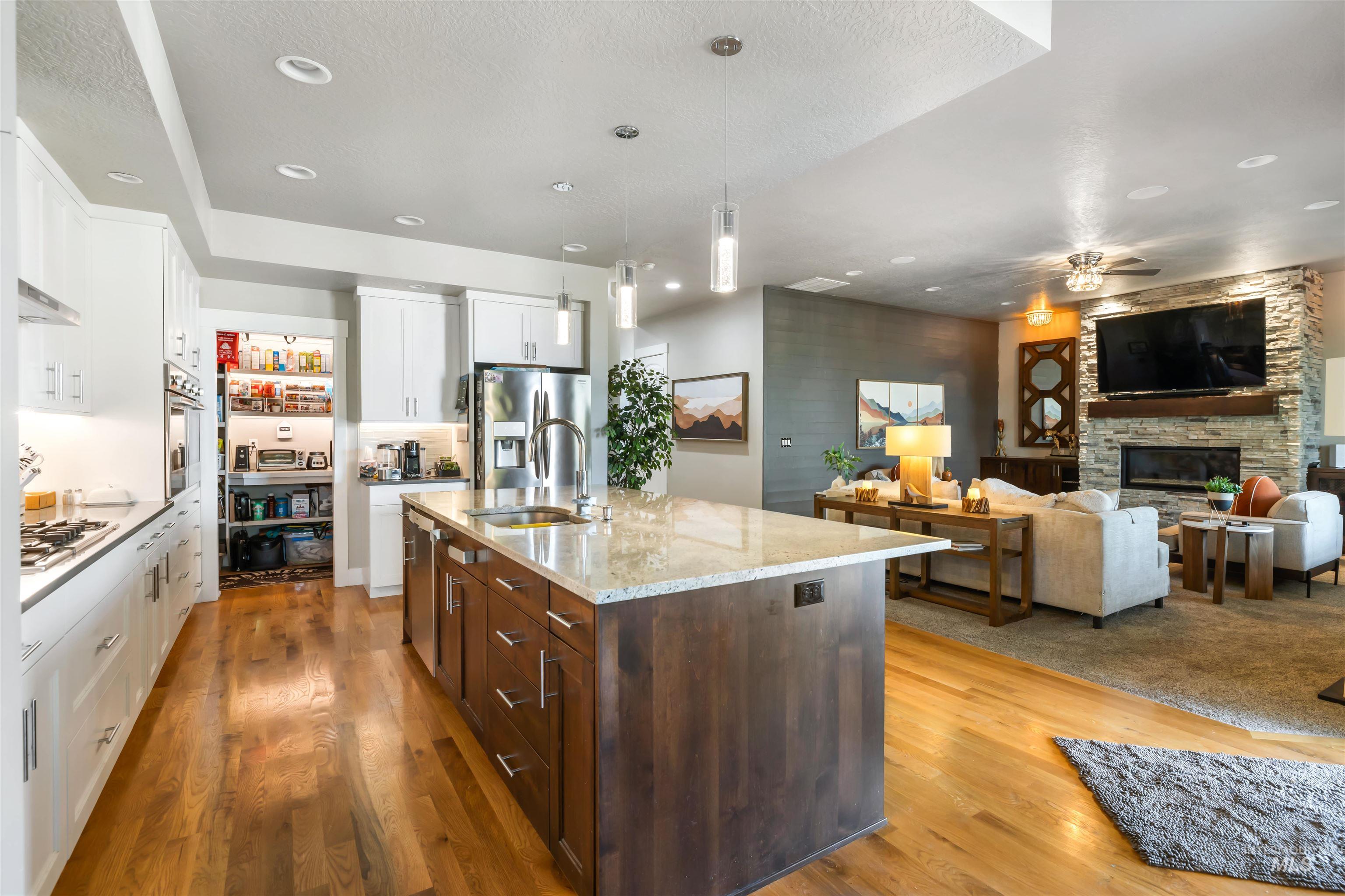 Kitchen with white cabinets, dark brown cabinets, pendant lighting, open floor plan, and a stone fireplace