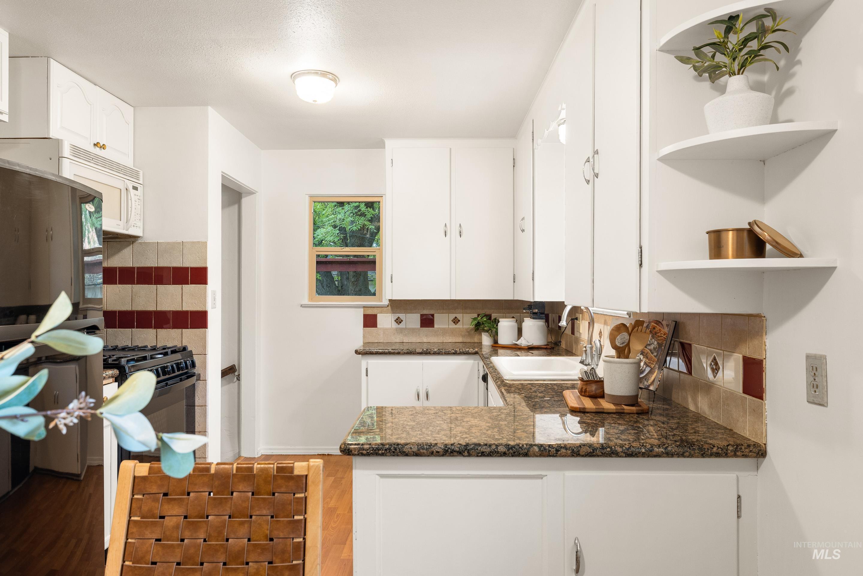 Kitchen featuring open shelves, white cabinets, decorative backsplash, and light wood-style floors