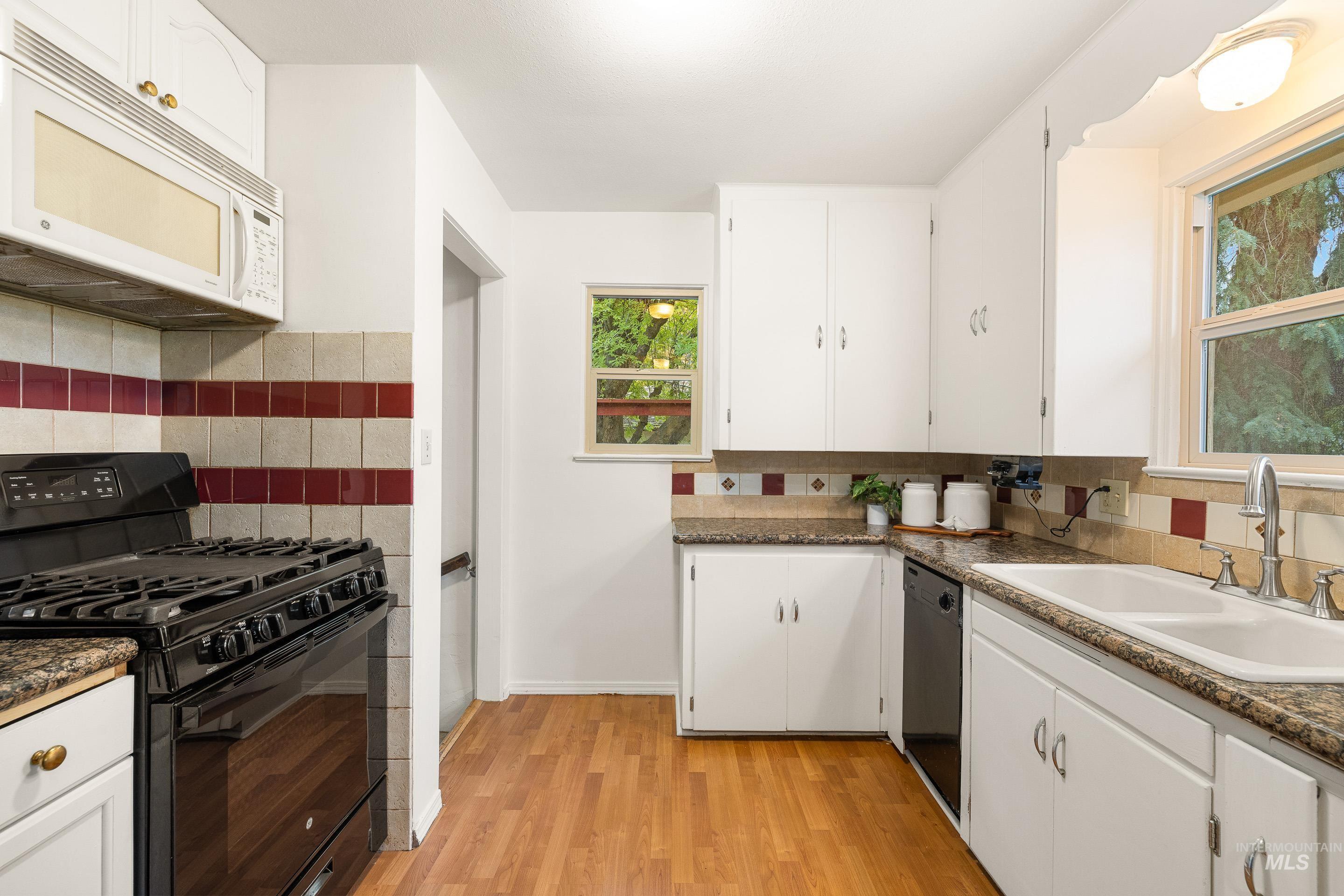 Kitchen featuring black appliances, white cabinetry, backsplash, and light wood finished floors