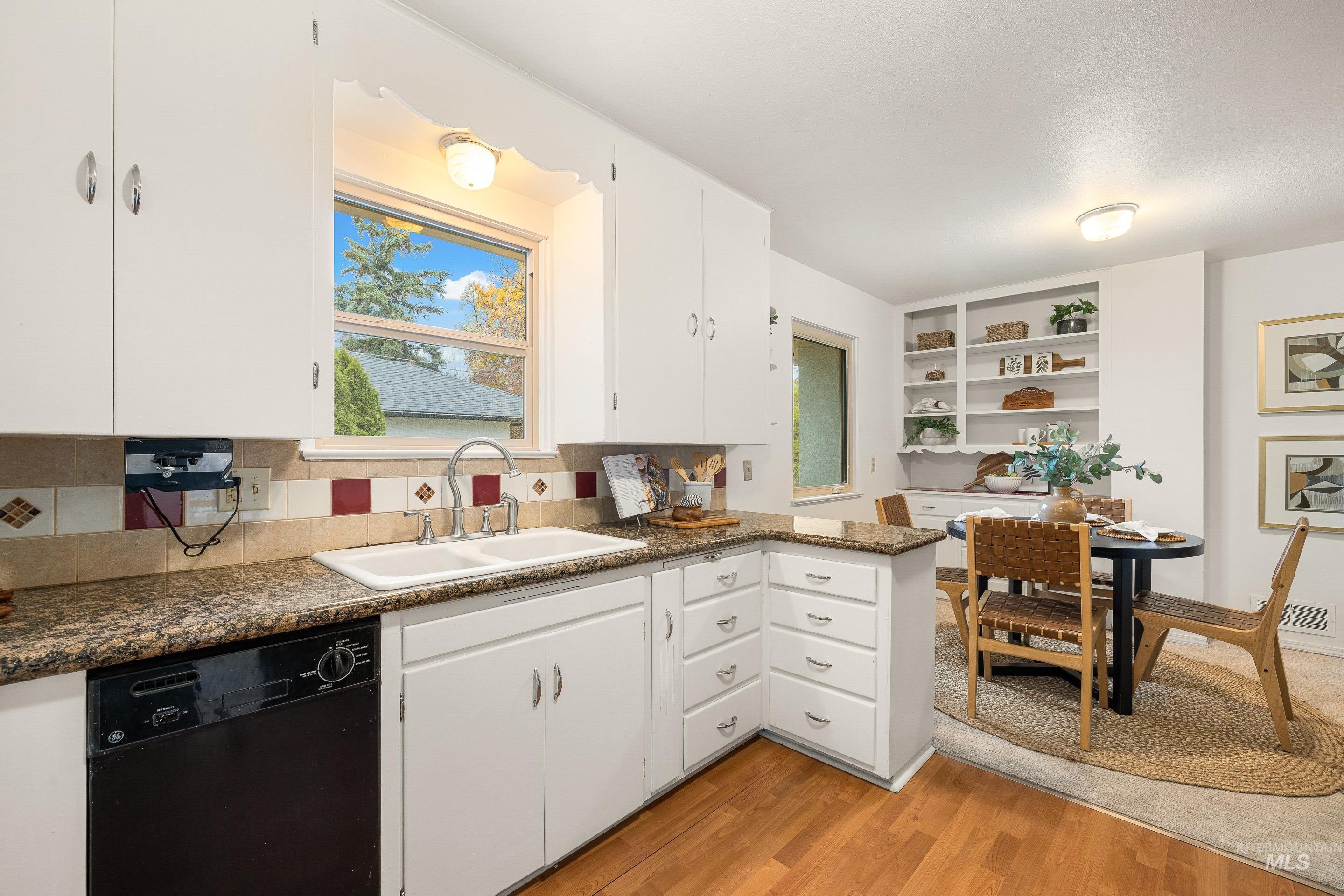 Kitchen with black dishwasher, white cabinets, light wood-type flooring, a peninsula, and tasteful backsplash