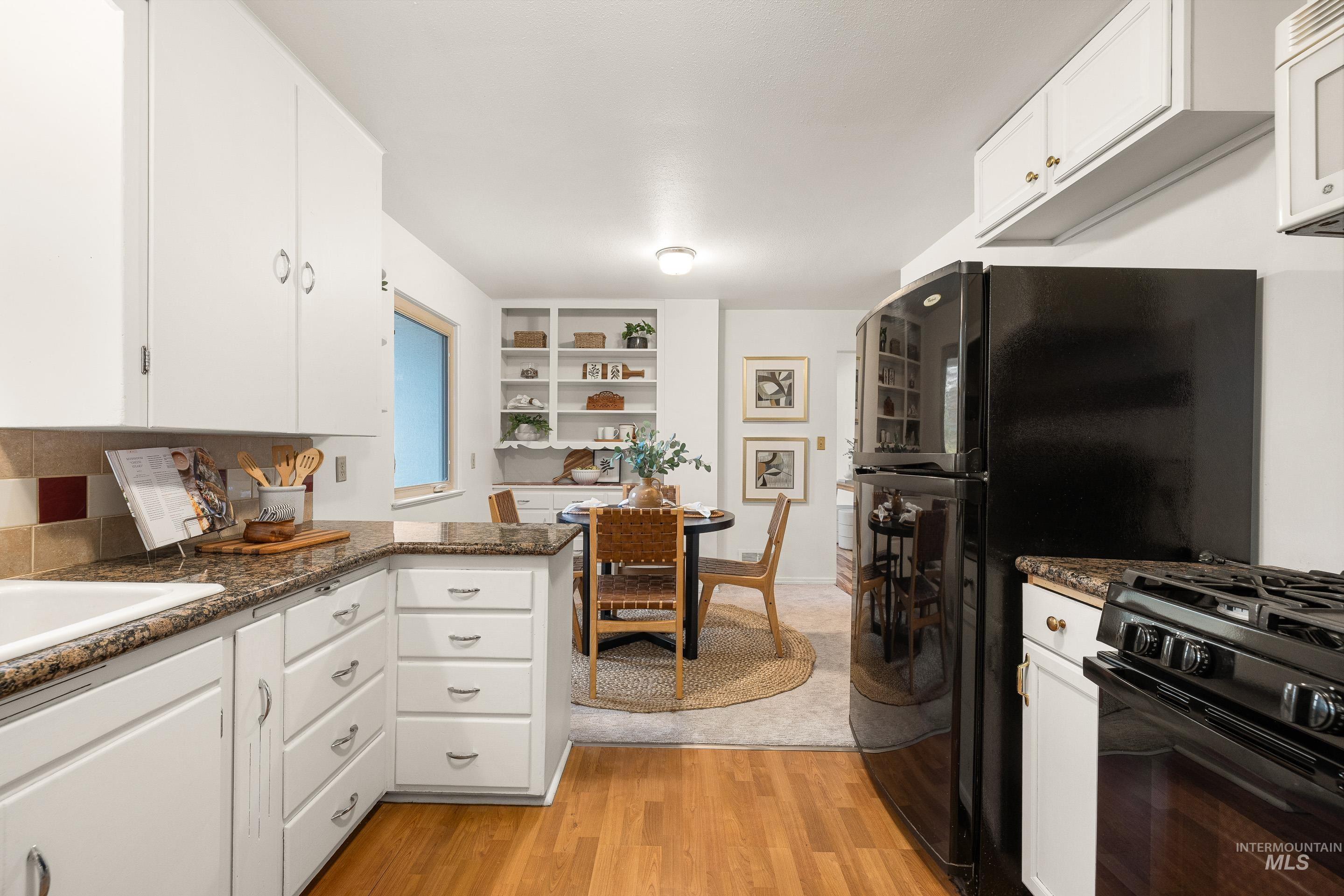 Kitchen featuring white cabinets, light wood-style flooring, white microwave, and a peninsula