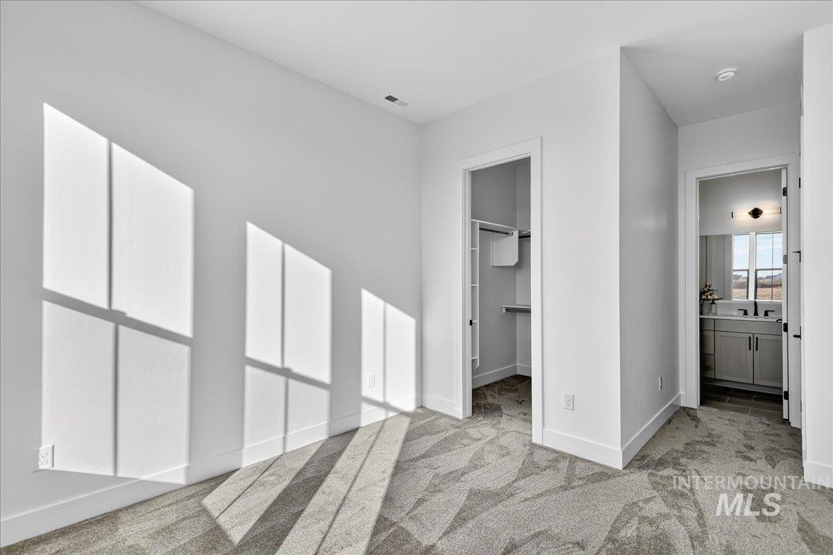 Unfurnished bedroom with a walk in closet, light carpet, and ensuite bath