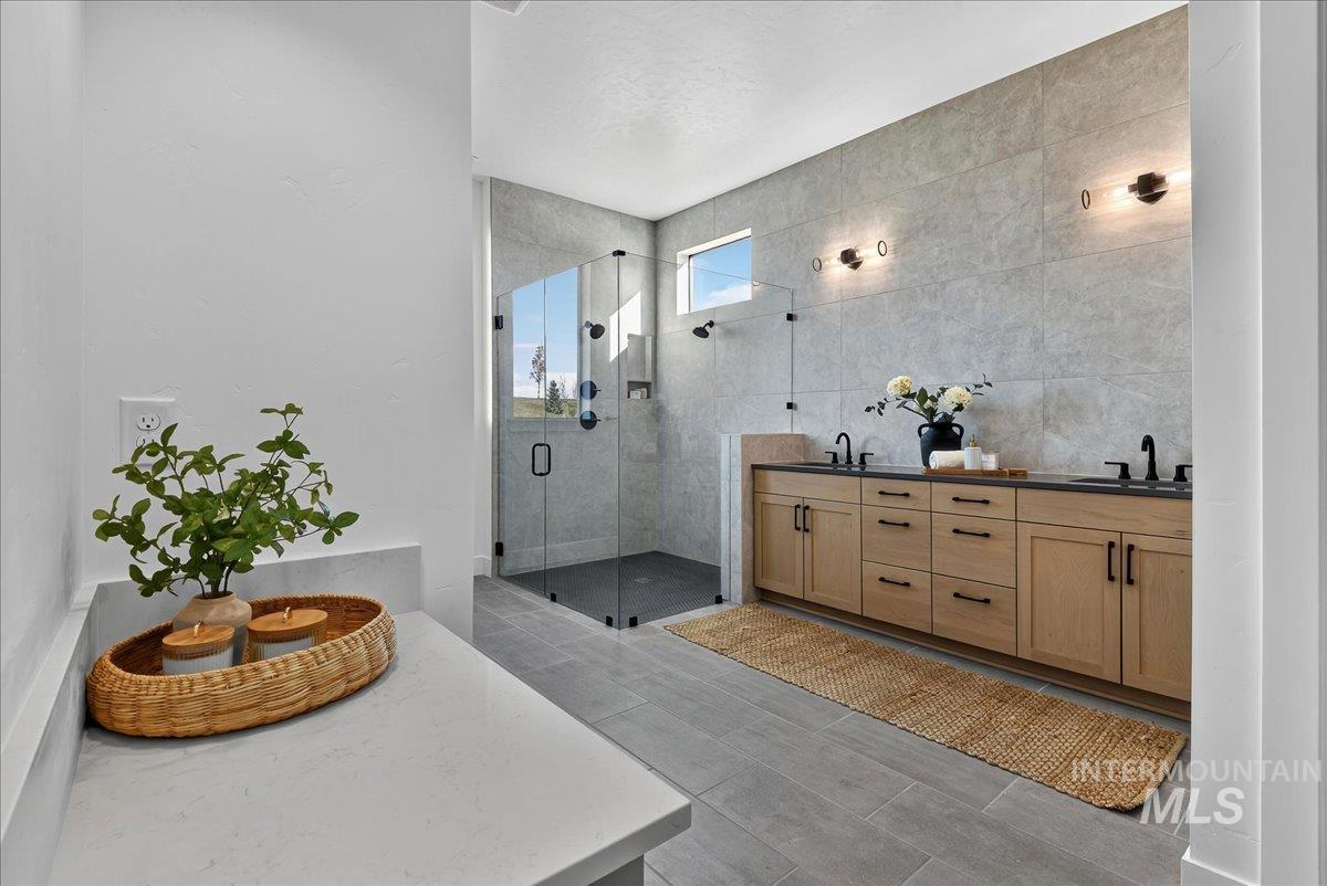 Full bathroom featuring double vanity, tile walls, and a stall shower
