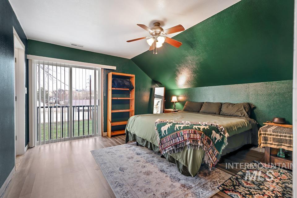 Bedroom featuring access to exterior, a textured wall, wood finished floors, vaulted ceiling, and ceiling fan
