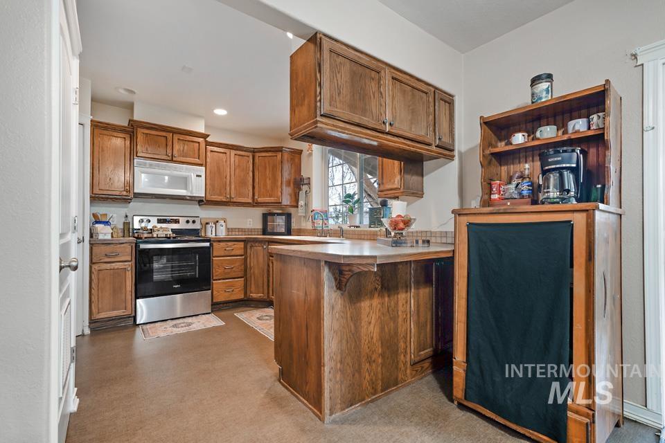 Kitchen featuring brown cabinets, stainless steel range with electric stovetop, white microwave, a kitchen bar, and a peninsula