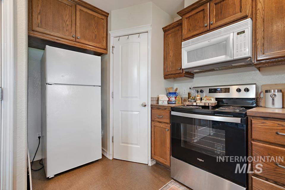 Kitchen with white appliances, brown cabinetry, and light countertops
